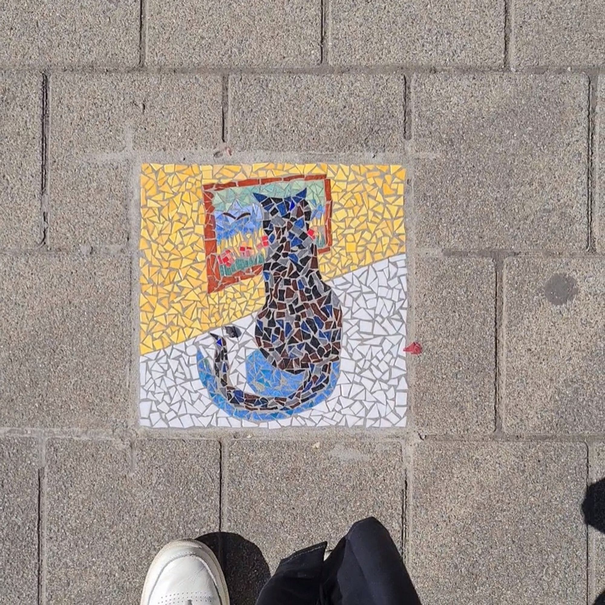 A mosaic tile of a cat set into the path