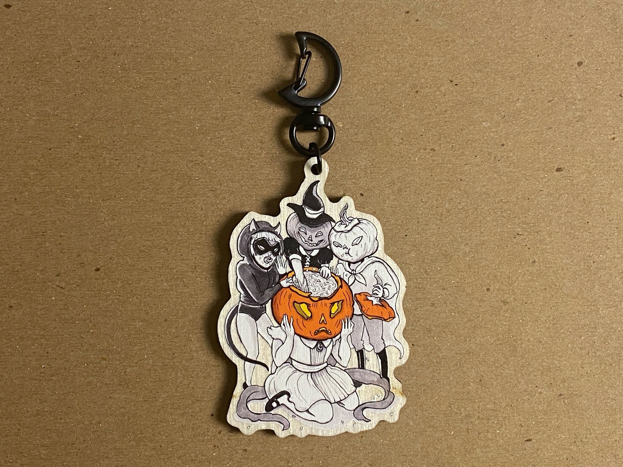 Vintage style Halloween illustration on a synthetic wooden keychain. Art is a black and white image of three costumed children gorging themselves on the pumpkin seeds from a jack o lantern child.