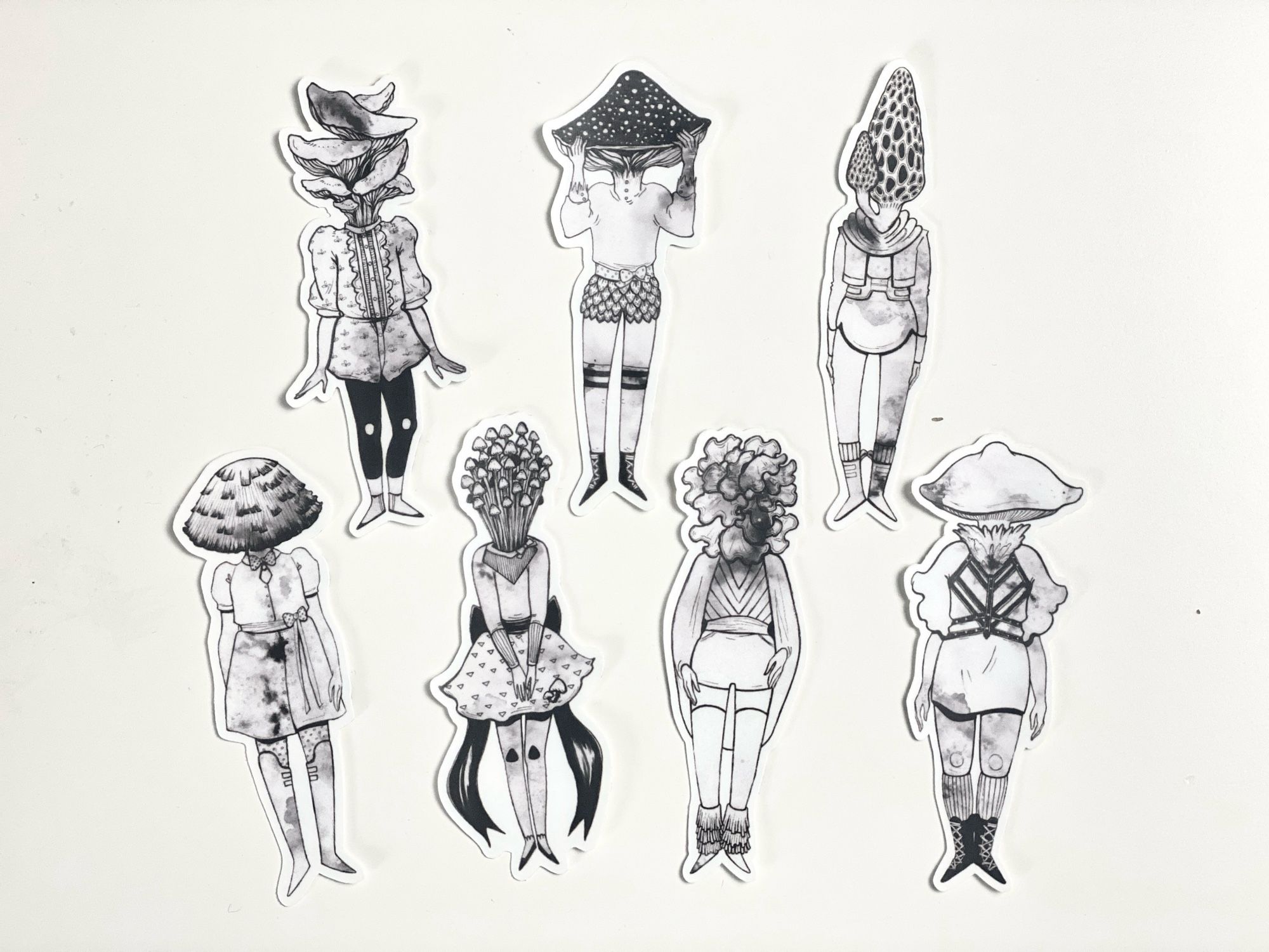 Seven little mushroom friends stickers. Each sticker is black and white pen drawing with cute little outfits. One each of Amanita, woodear, fairyring, morel, enoki, oyster and ink cap mushrooms.