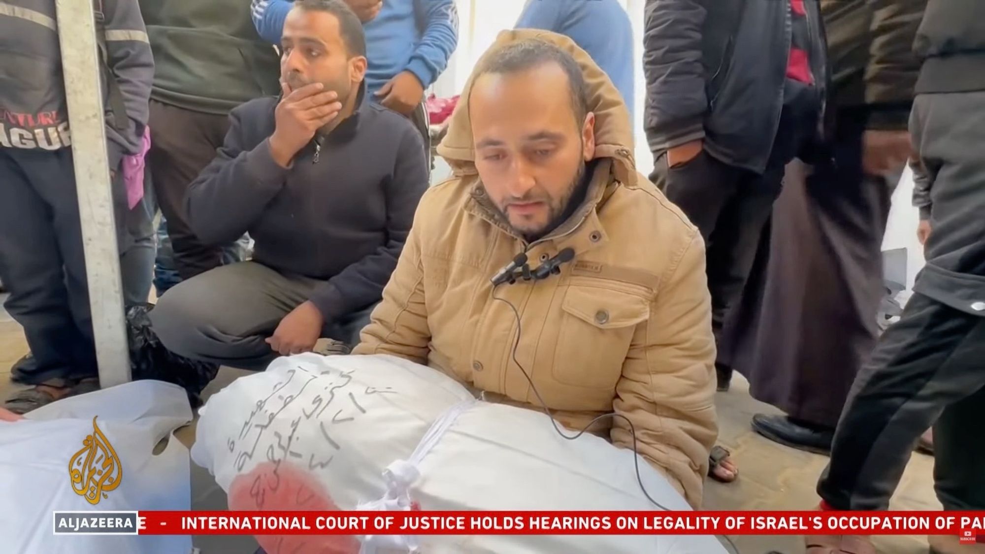 A Palestinian man Abdurrahman holding his daughter’s body wrapped in a white sheet with writing on it and a blood stain.