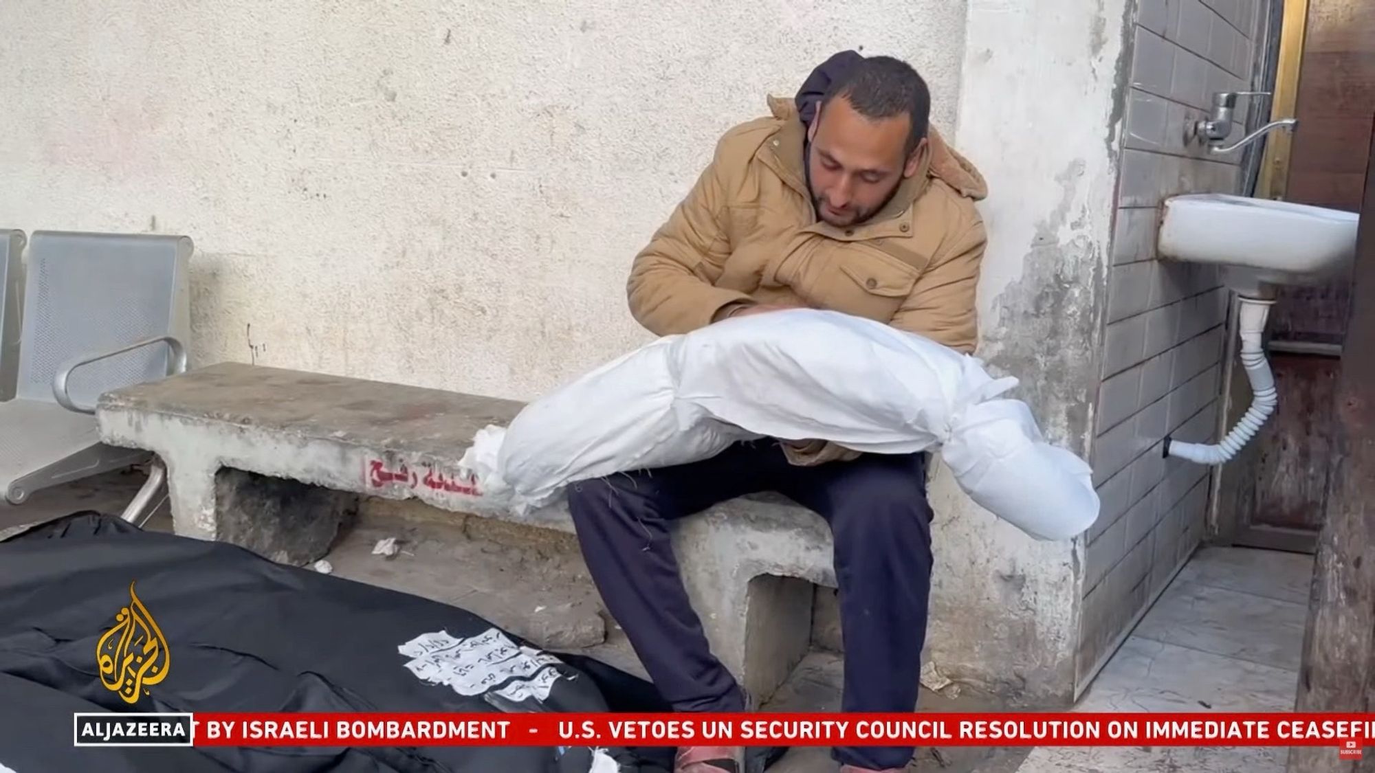 A Palestinian man Abdurrahman holding his daughter’s body wrapped in a white sheet with writing on it and a blood stain.