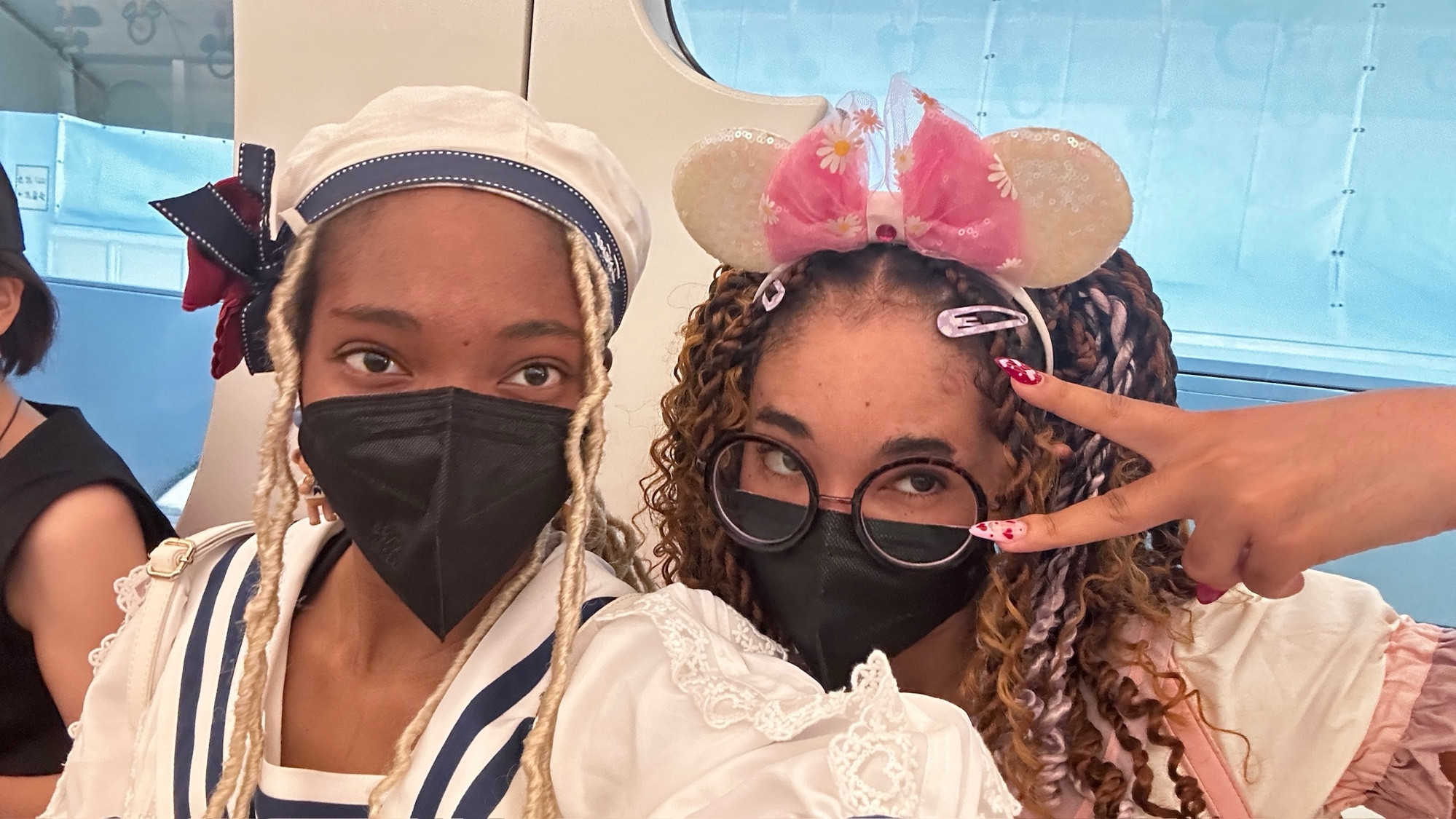 Me and my best friend wearing face masks on the Disney Monorail. I am on the left wearing a sailor hat and sailor blouse with my blonde locs, while my friend is wearing glasses, has braids, and is wearing a sailor One Piece dress. 