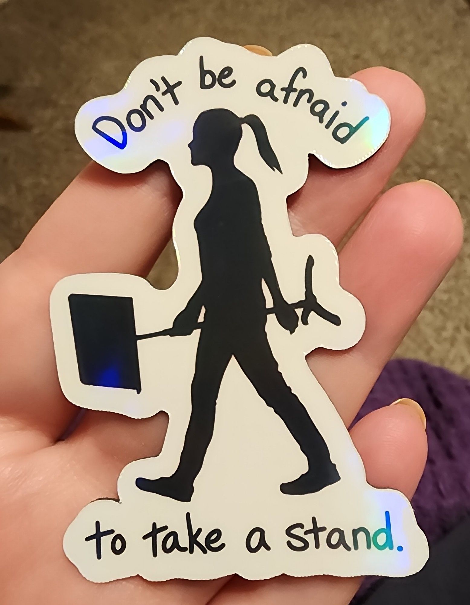 A sticker of a girl holding a music stand, words read: don't be afraid to take a stand