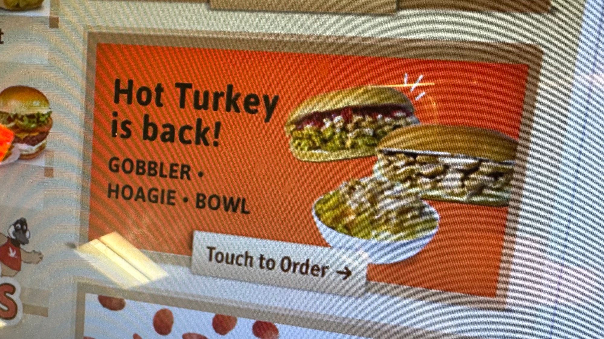 Close-up photo of a Wawa ordering kiosk, the touch screen showing an advertisement that “Hot Turkey is back!” With options for a Gobbler, hoagie, or bowl.