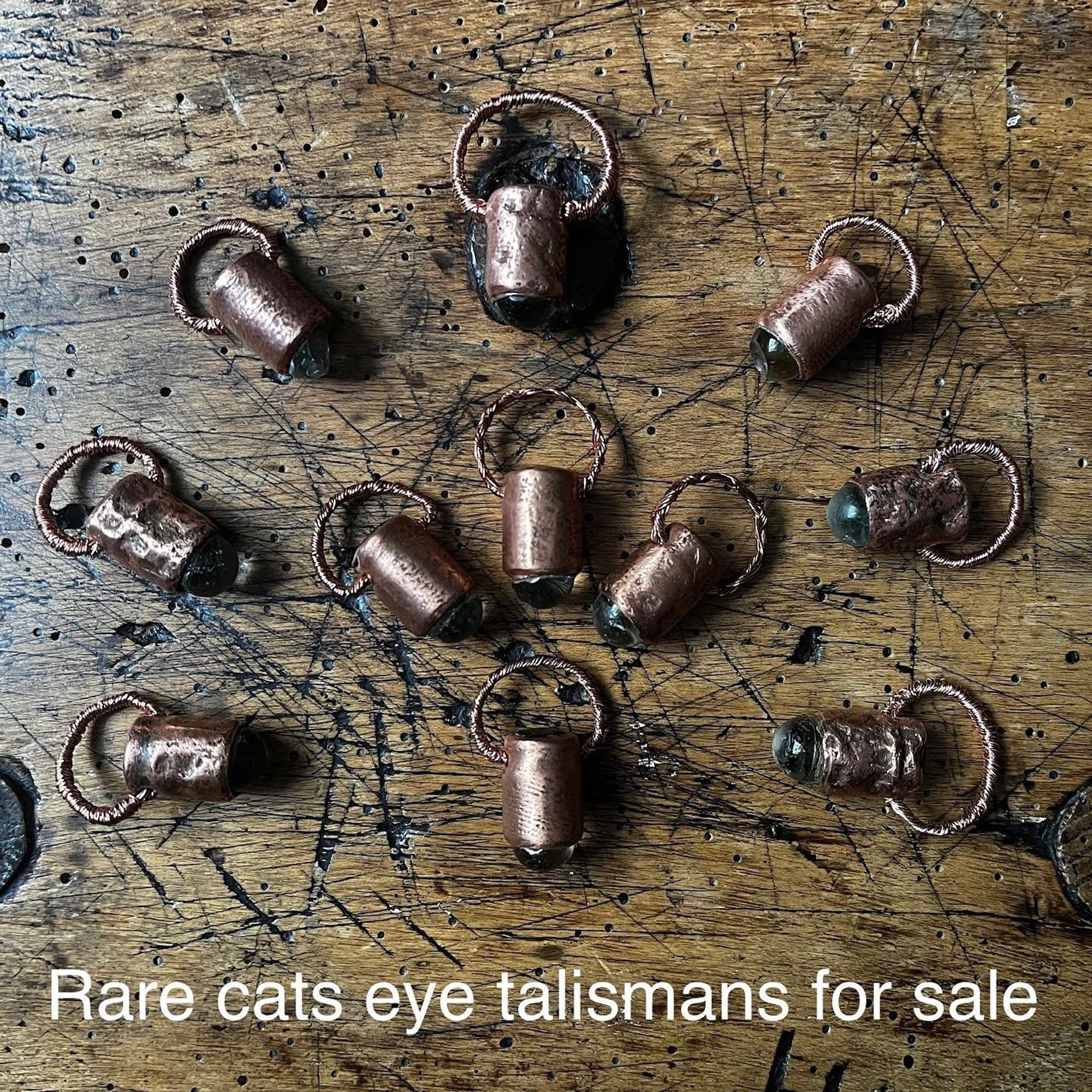 Image shows 11 bullet-shaped copper pendants with large round copper bails, they are inset with clear glass spheres, some are more weathered than others. Text reads 'rare cats eye talismans for sale'. They are really cool and you should definitely buy one.