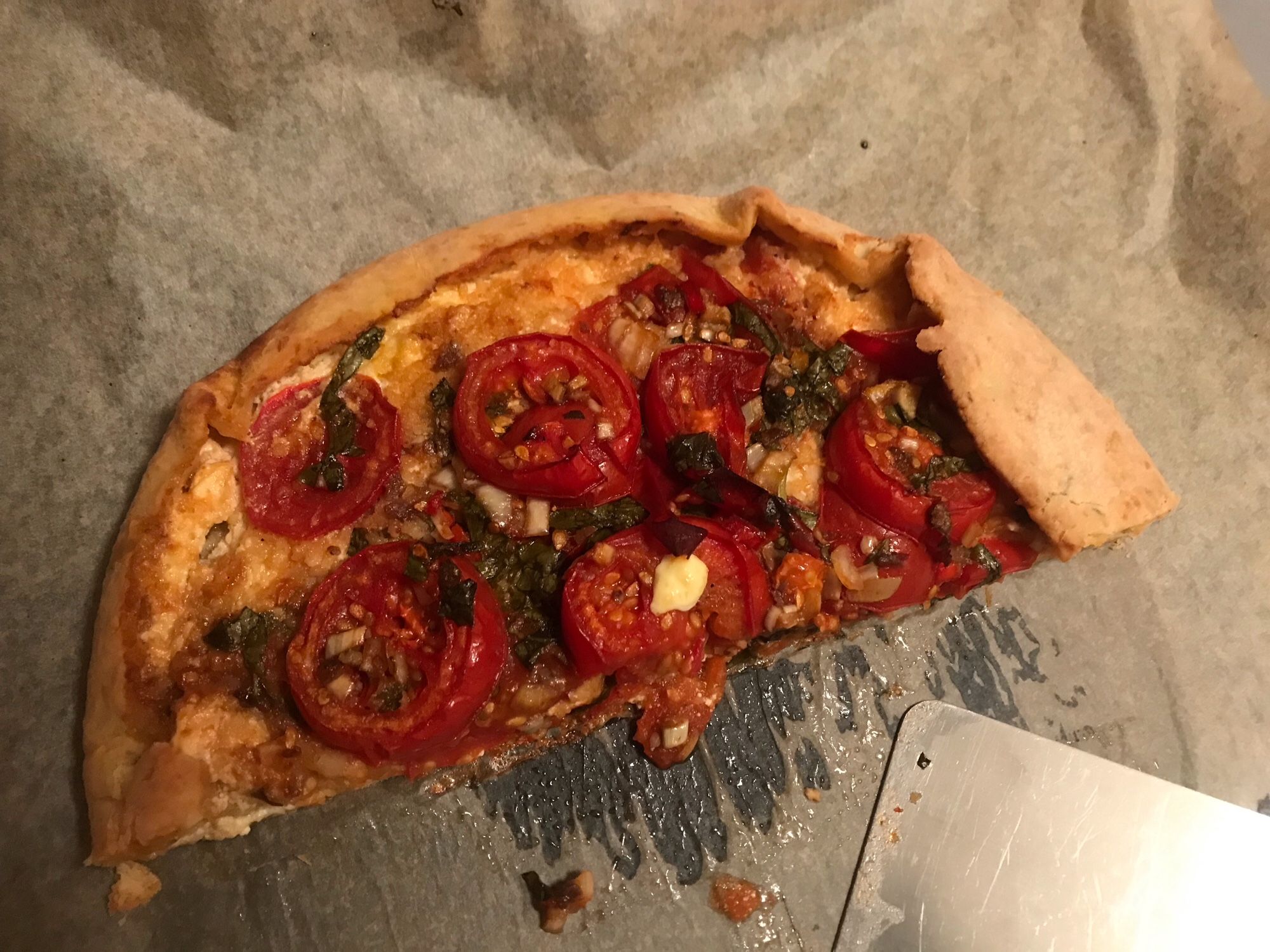 Eine gebackene, am Rand hochgeklappte halbe Mürbeteigplatte belegt mit Tomatenscheiben auf Backpapier.