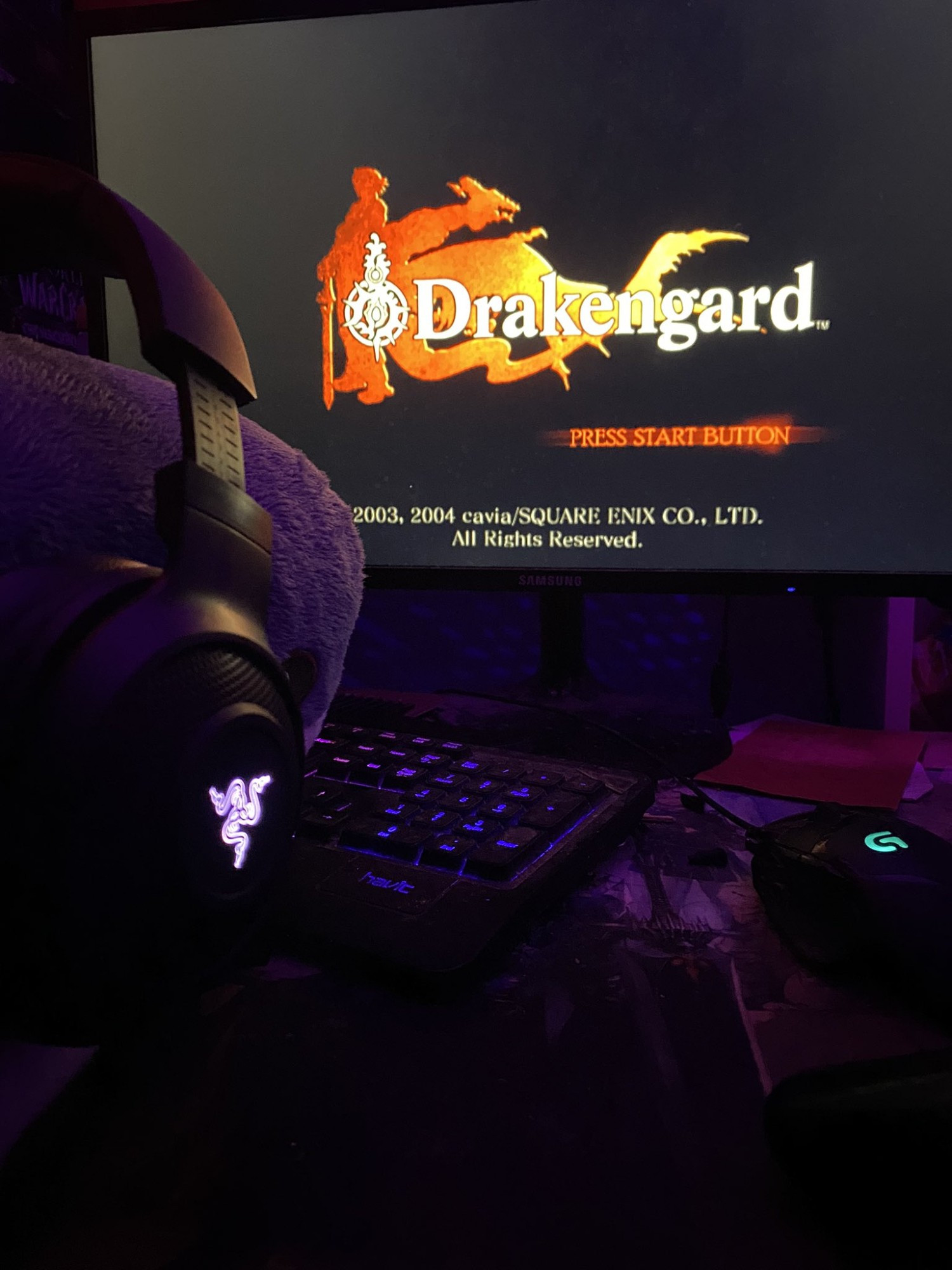 Picture of Blåhaj looking at a screen displaying the Drakengard logo. Blåhaj is wearing a headset