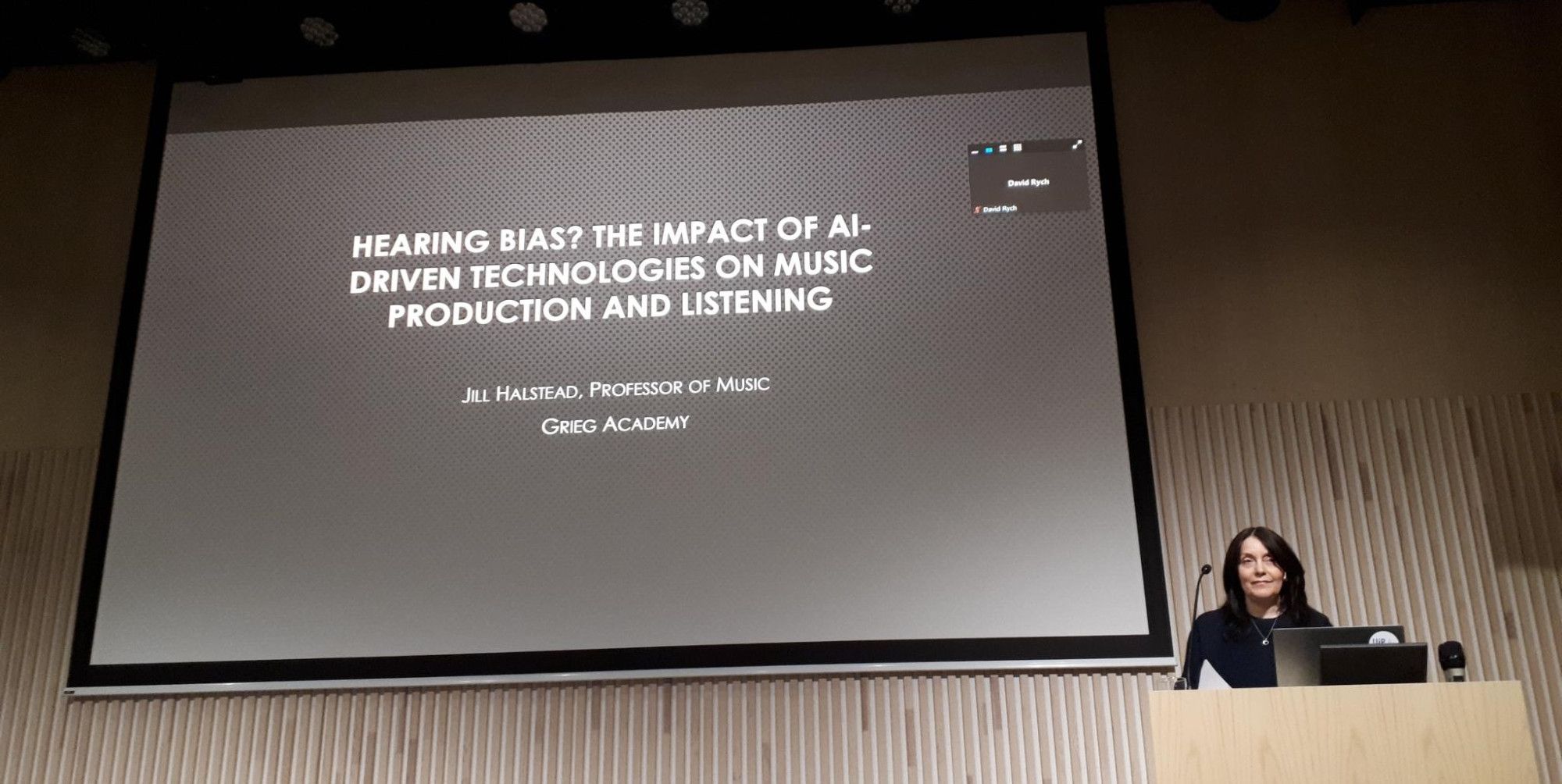 A woman giving a presentation with the title Hearing bias? The impact of AI-driven technologies on music production and listening.