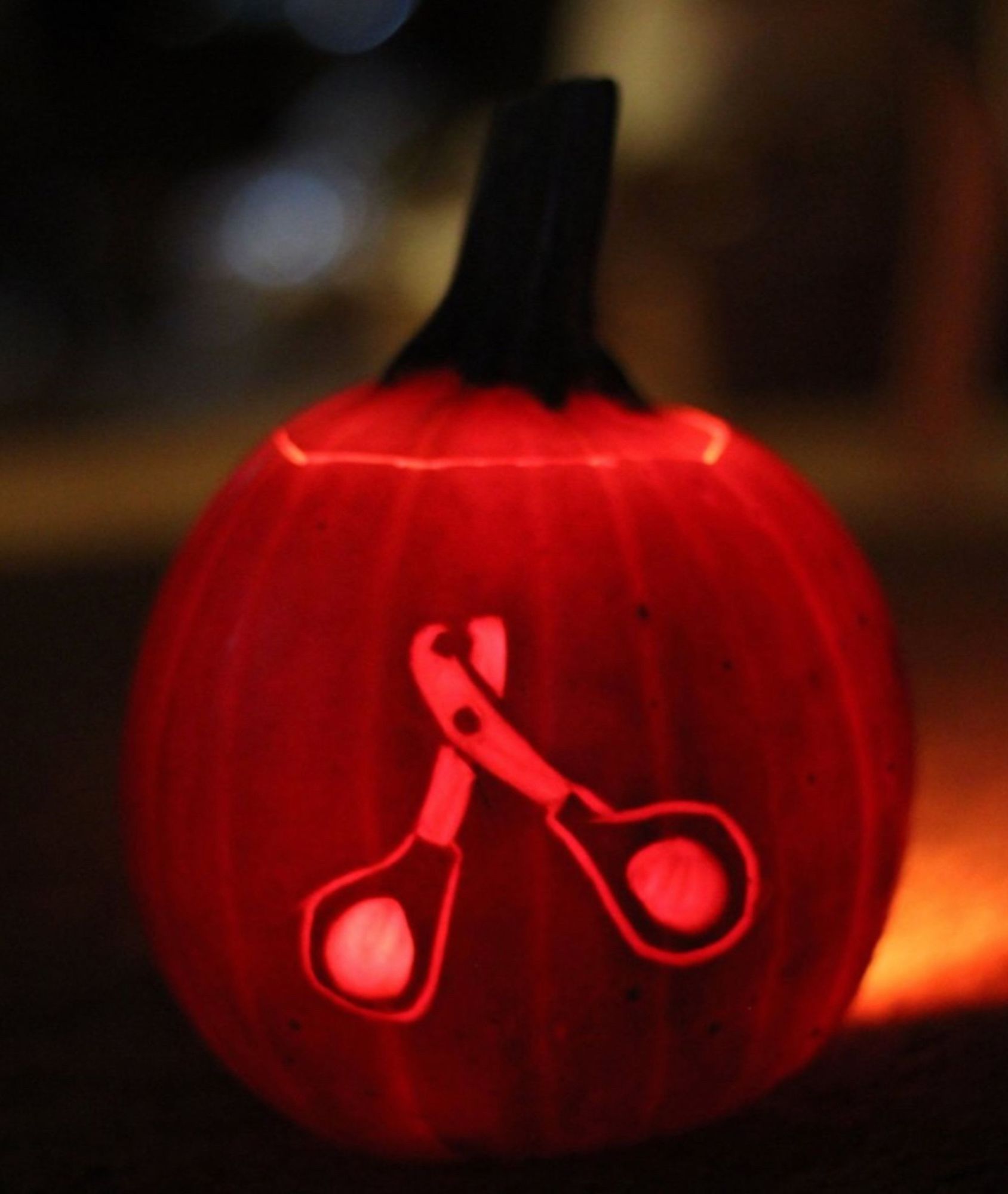 An orange mini pumpkin with scissor-type pet nail trimmers carved into it. It's dark and the pumpkin is illuminated from within.