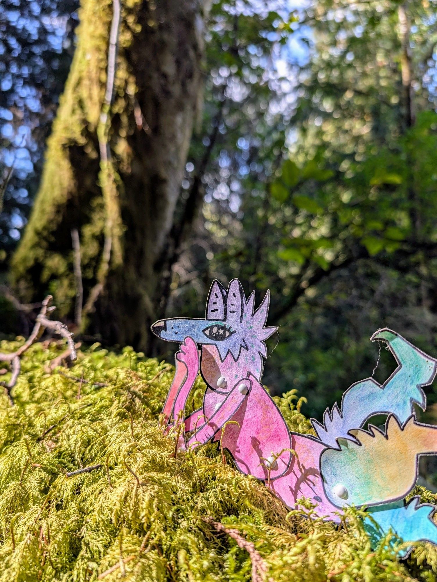 A colorful paper coyote character lies on their stomach on a bed of green moss