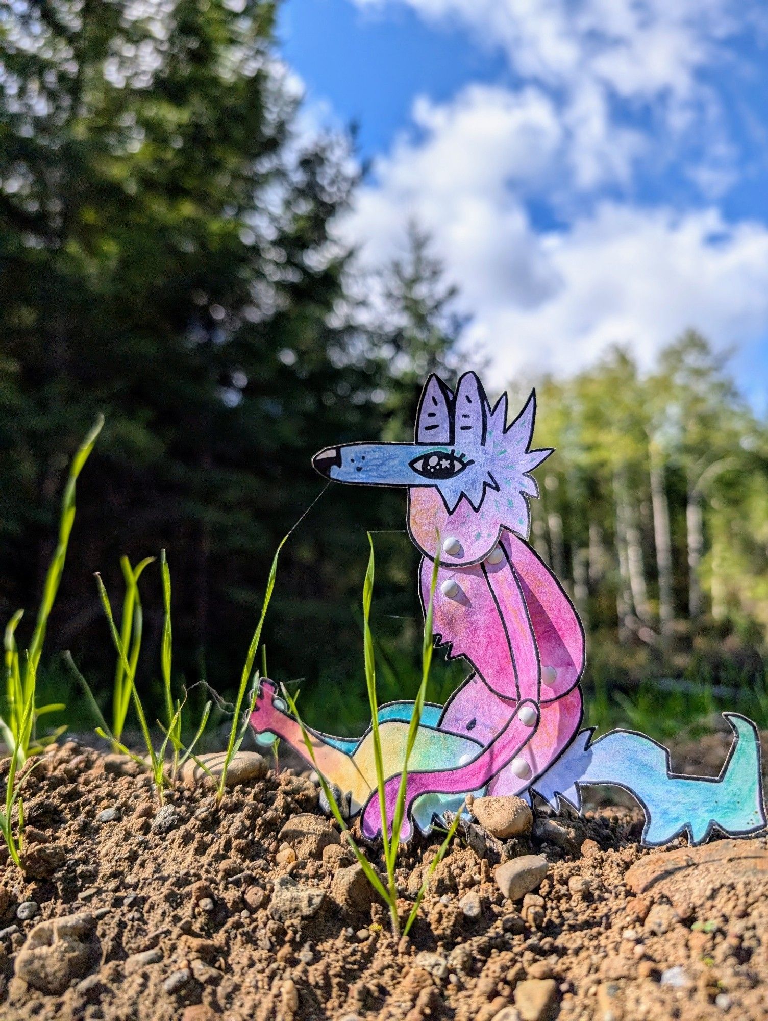 A colorful paper coyote character sitting outside on a sunny day in the woods