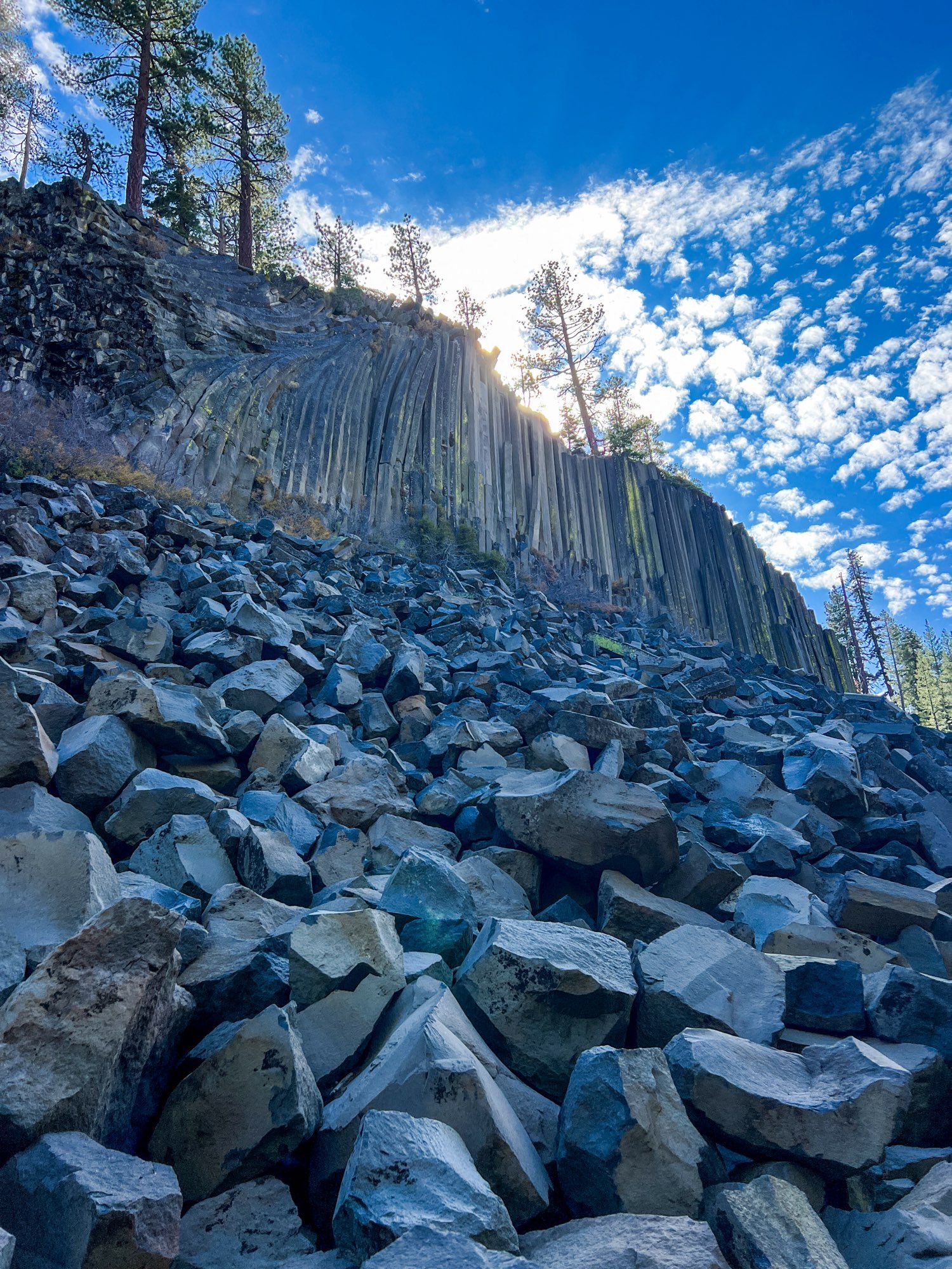 A view looking southeast upwards at Devil Postpile. There are multiple columns of hexagon basalt columns with a large boulder field in the foreground. The sky is mixed clear and cloudy.

From Wikipedia:

The Postpile's columns average 2 feet (0.61 m) in diameter ("The columns vary in size from ten to 30 inches in diameter."[3]), the largest being 3.5 feet (1.1 m), and many are up to 60 feet (18 m) long.
Together they look like tall posts stacked in a pile, hence the feature's name. If the lava had cooled perfectly evenly, all of the columns would be expected to be hexagonal, but some of the columns have different polygonal cross-sections due to variations in cooling.