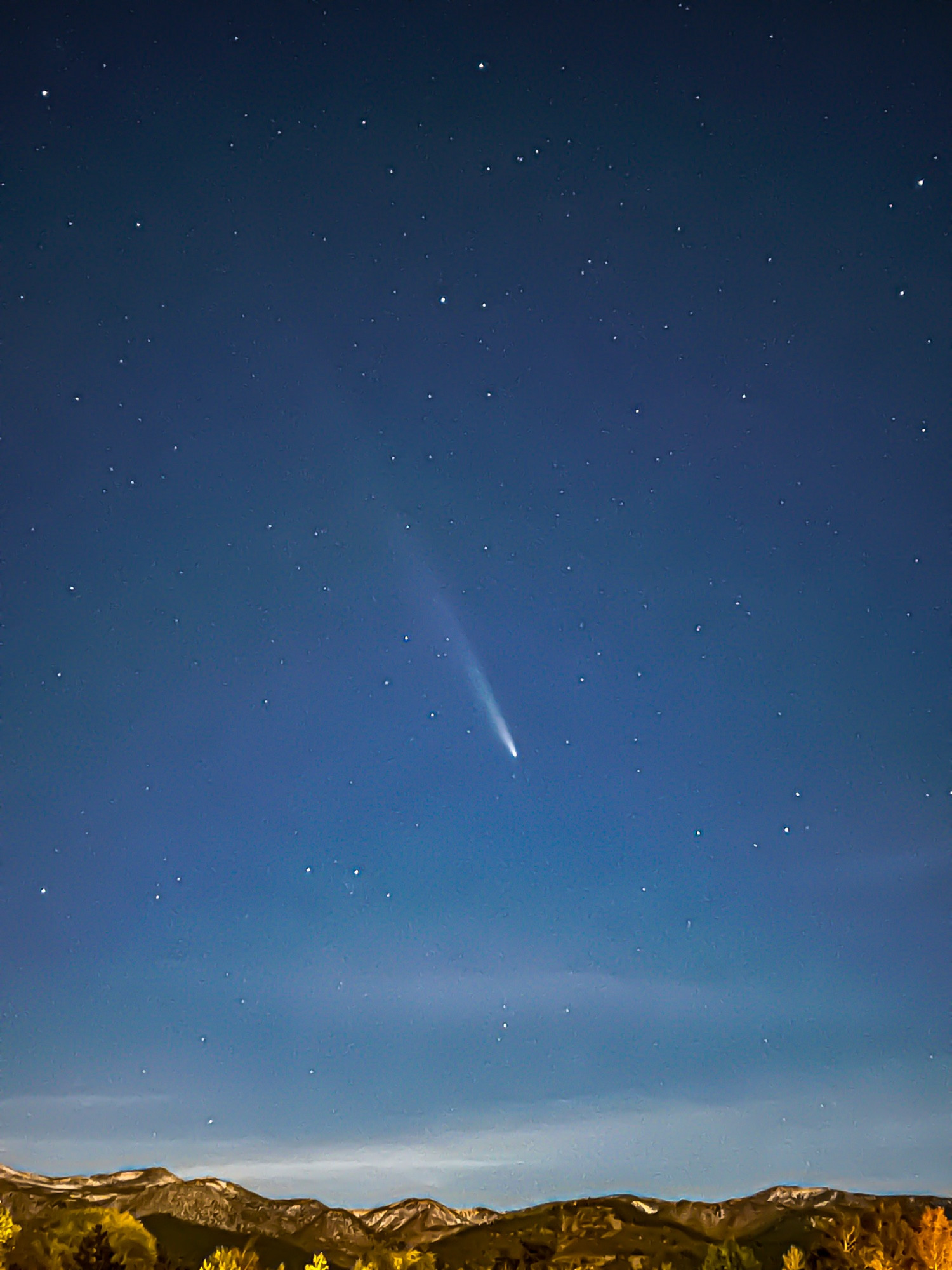 A comet above hills that have thin smeary clouds resting on them. 