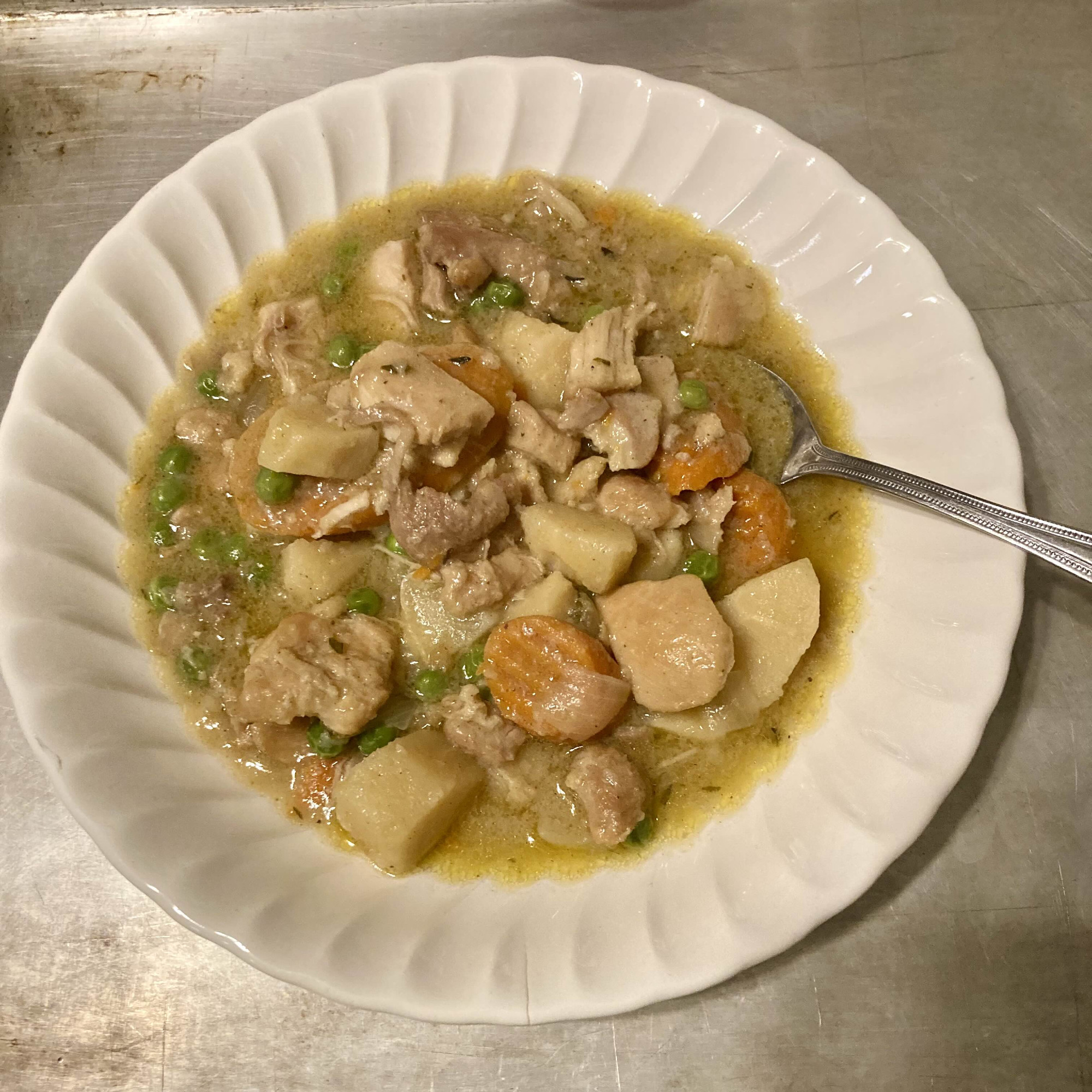 a shallow white bowl with chicken stew with chunks of parsnips, carrots, and some peas flotting around. there's a shimmer of fat on the gravy but not too much 