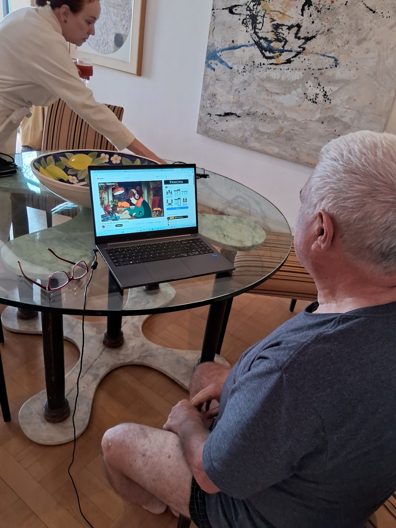 My father in his pyjamas watching a laptop with the lofi hip hop radio channel running and my mom in the background