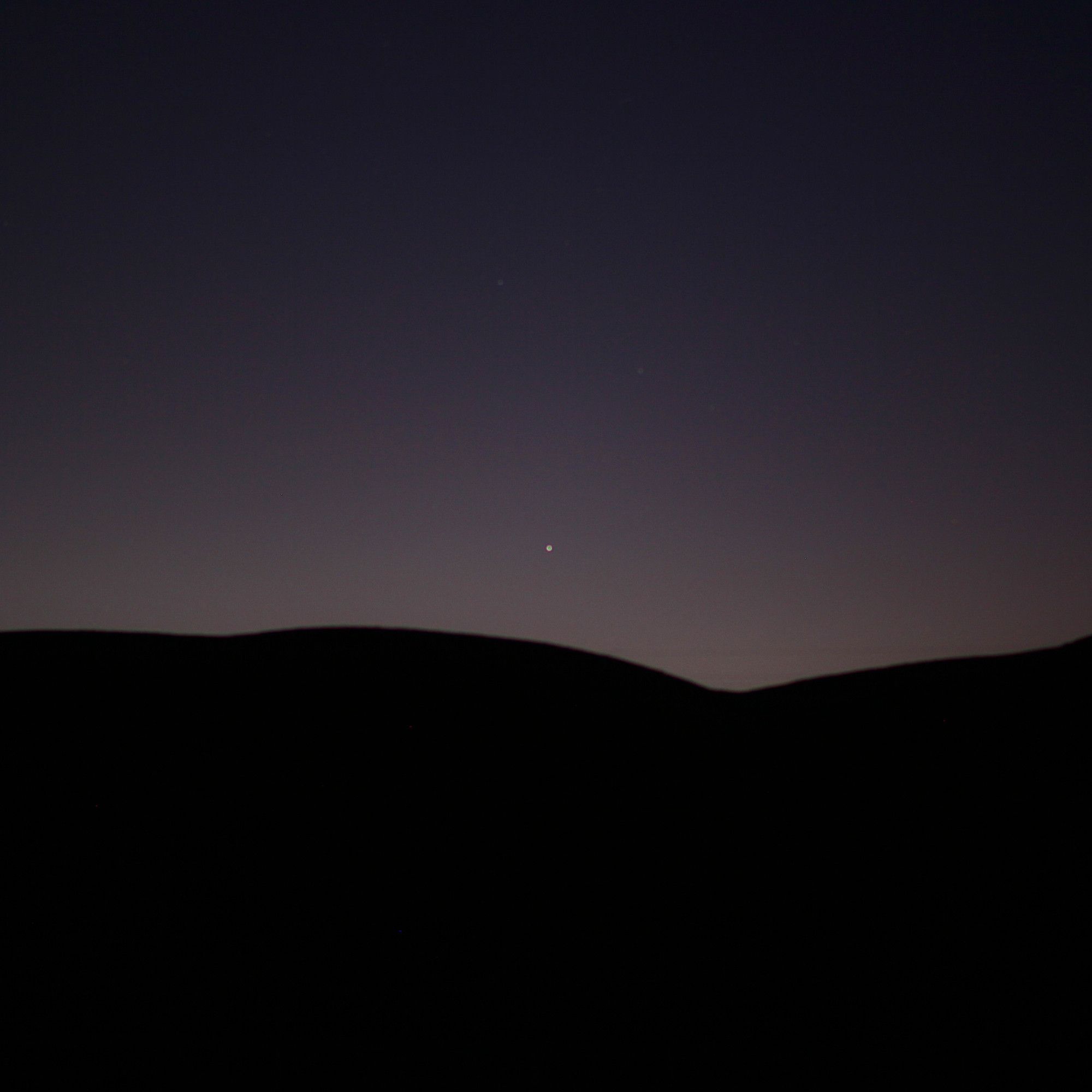 The horizon just before dawn, with the hills silhouetted in darkness, with a single bright point just a little bit above them in the glow of first light.