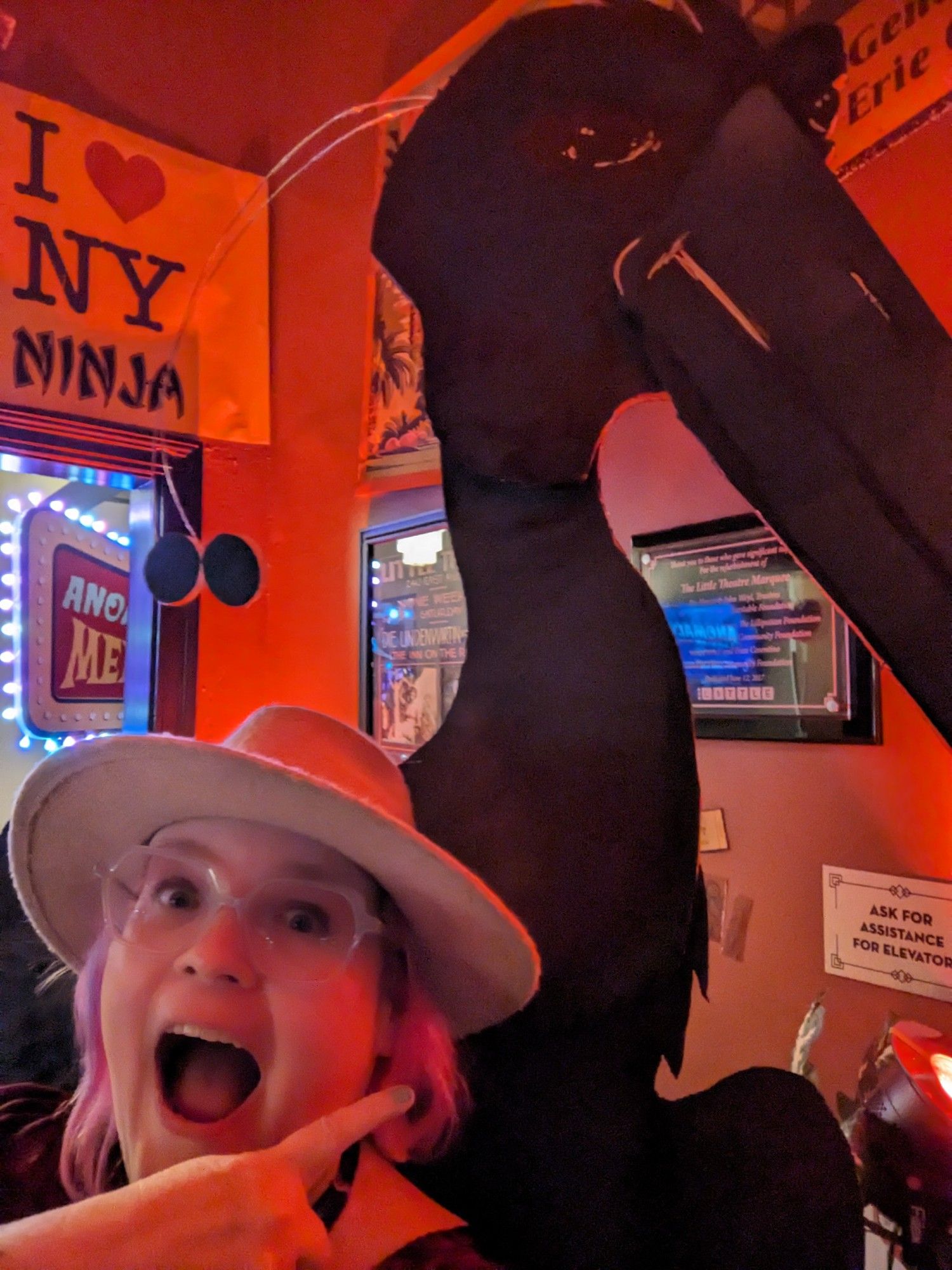 A selfie while yelling and pointing up at a terrifying, giant black bird standee.