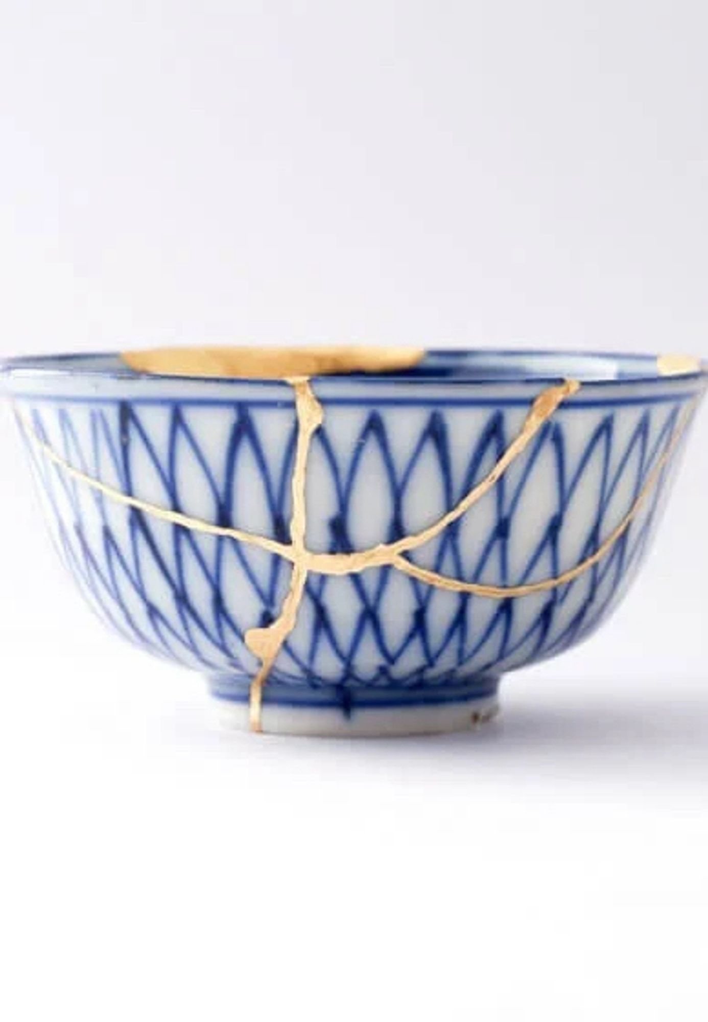 A blue and white rice bowl on a white background. The bowl has been repaired using the Japanese practice of kintsugi, so that the cracks show up in gold.