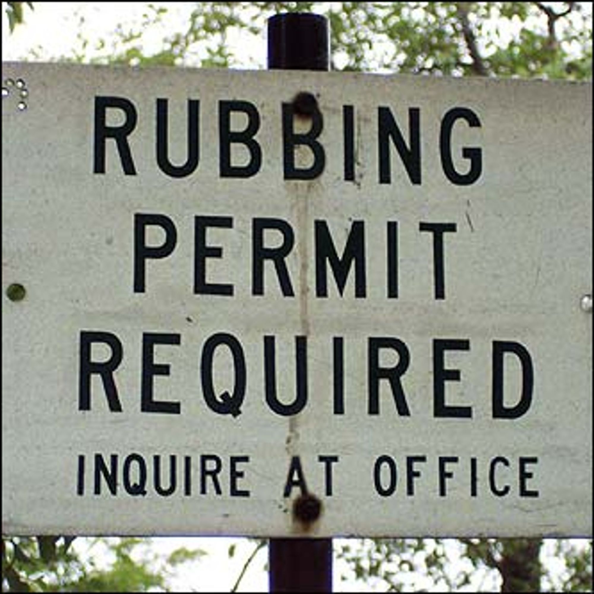 An old white sign with black lettering that says "RUBBING PERMIT REQUIRED" in large letters with "INQUIRE AT OFFICE" in smaller letter below. Presumably from a graveyard/cemetery but notable for the double entendre.