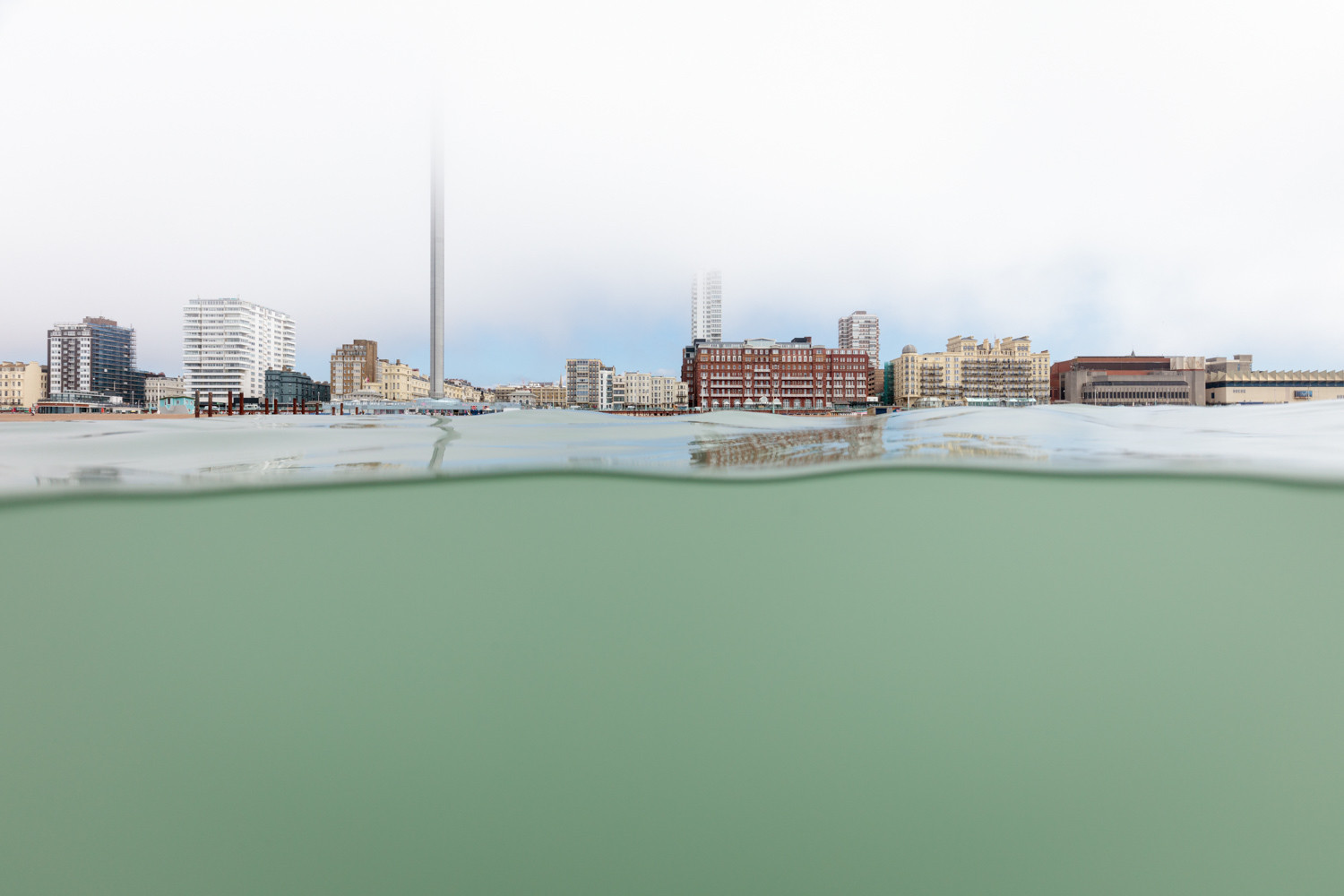 A photograph of Brighton seafront as seen from the sea. The camera is half in and half out of the water and low cloud is consuming the tops of the taller buildings. 