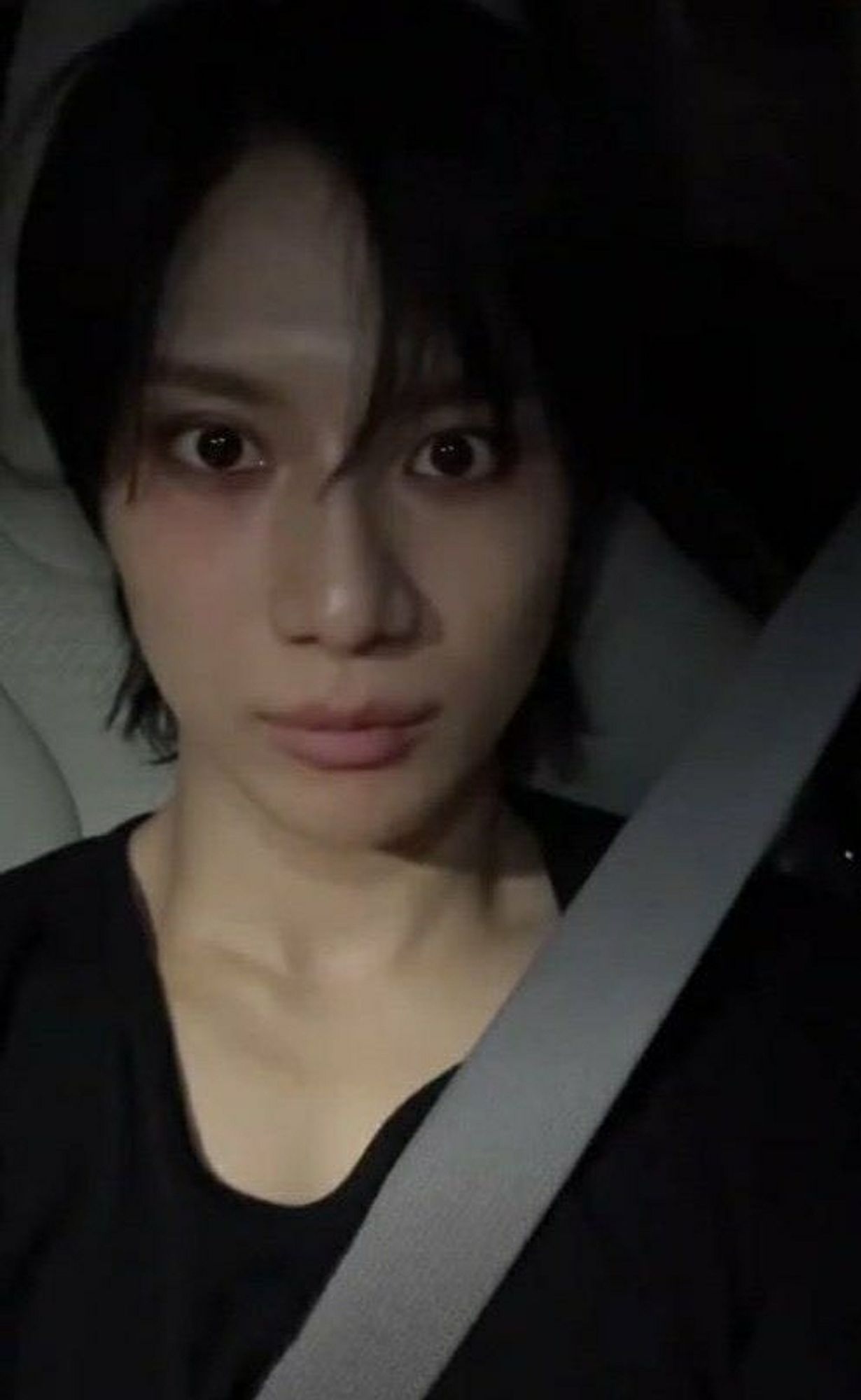 SHINee Taemin strapped in with seat belt. Black t-shirt with stretched collar. Staring vacant and despondent towards the camera. Blush under eyes gives off haunted Victorian waif vibes.