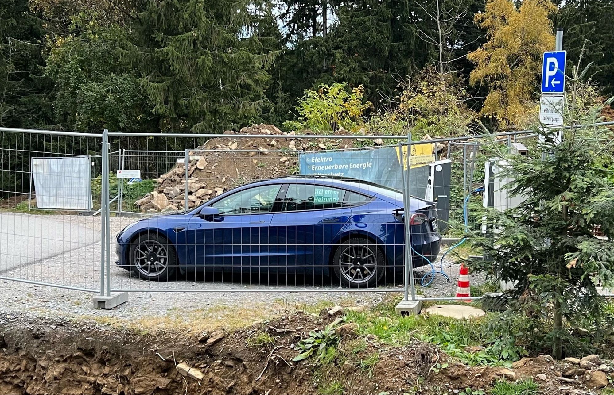 Mein blaues Tesla Model 3 an der Ladesäule des WaldWipfelWeges in St. Englmar. Vor dem Auto steht ein Bauzaun, der Anlass für den witzigen Spruch in Anlehnung an den Werbespot von Gilette Rasierern.