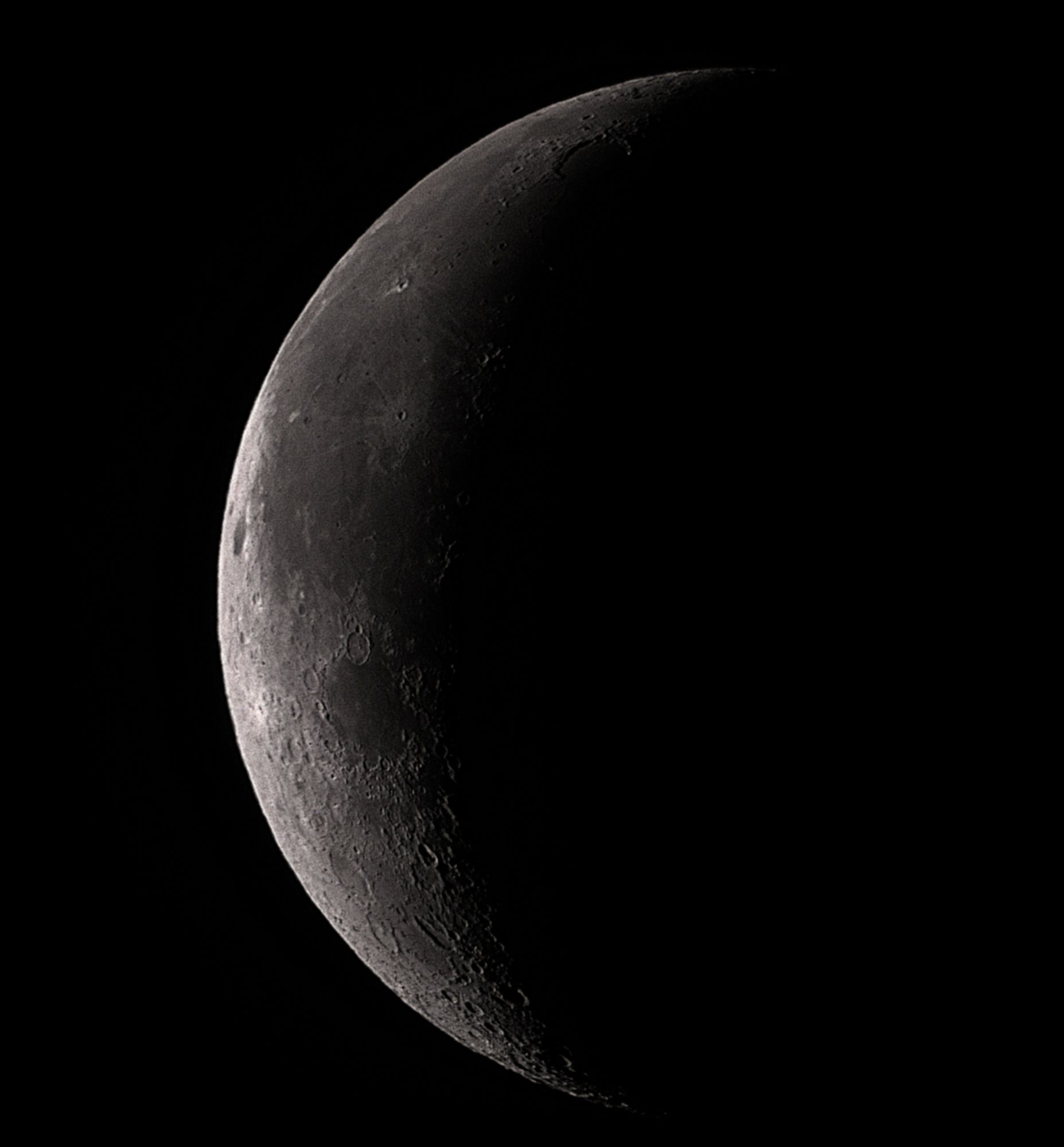 A telescopic image of a waning crescent Moon showing dark, vast lava plains and many impact craters.