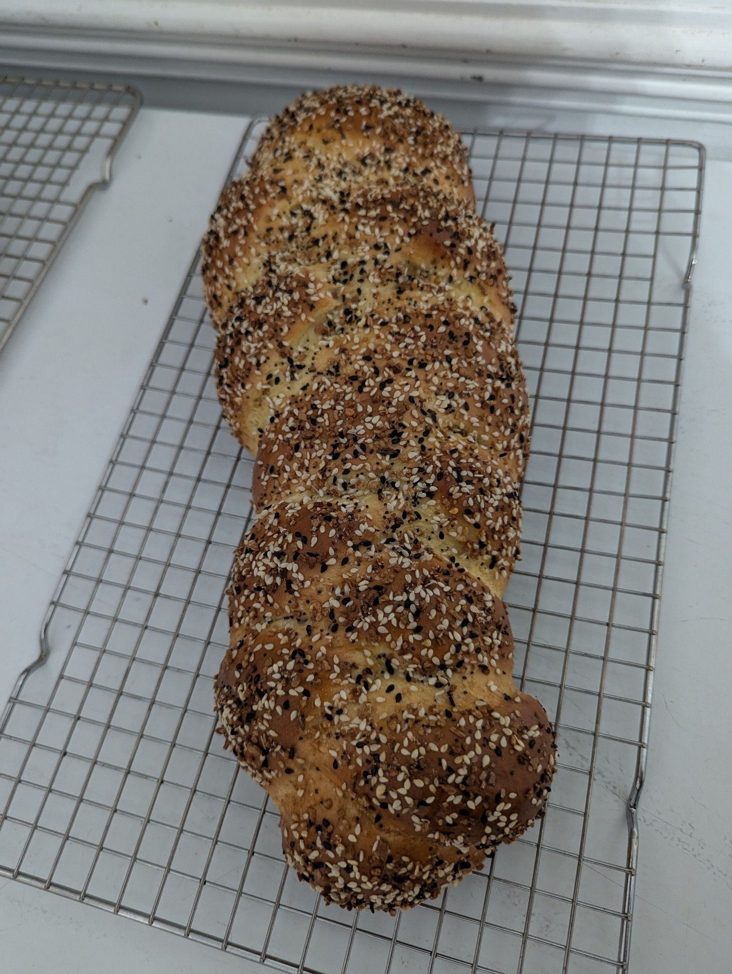 3-strand challah topped with everything bagel season cooling on a wire rack on top of a chest freezer