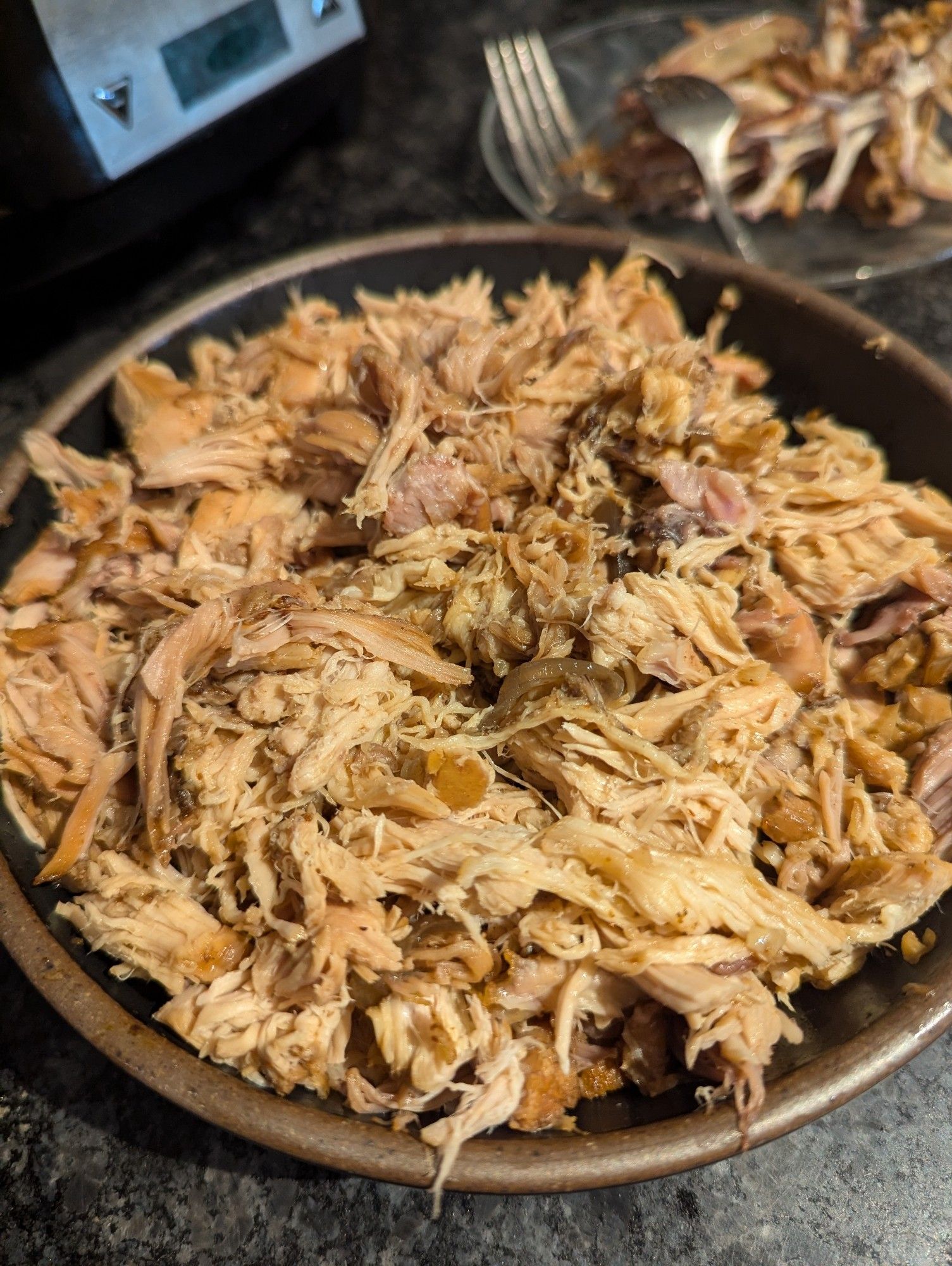 Shredded rabbit meat in a bowl on a counter, behind the bowl is a blurry picture of forks and bones on a plate