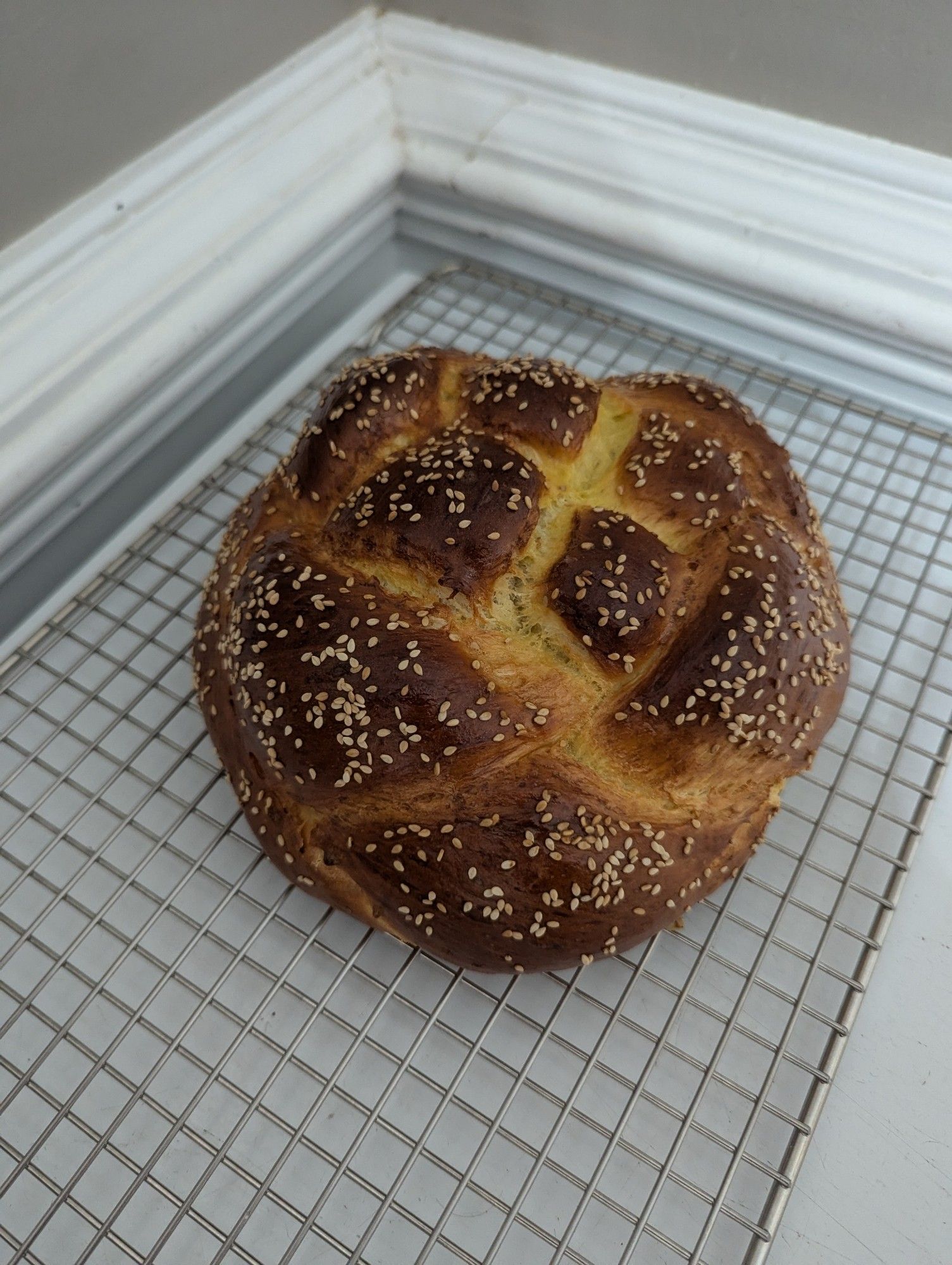 Round challah topped with sesame seeds cooling on a wire rack in a corner on a chest freezer