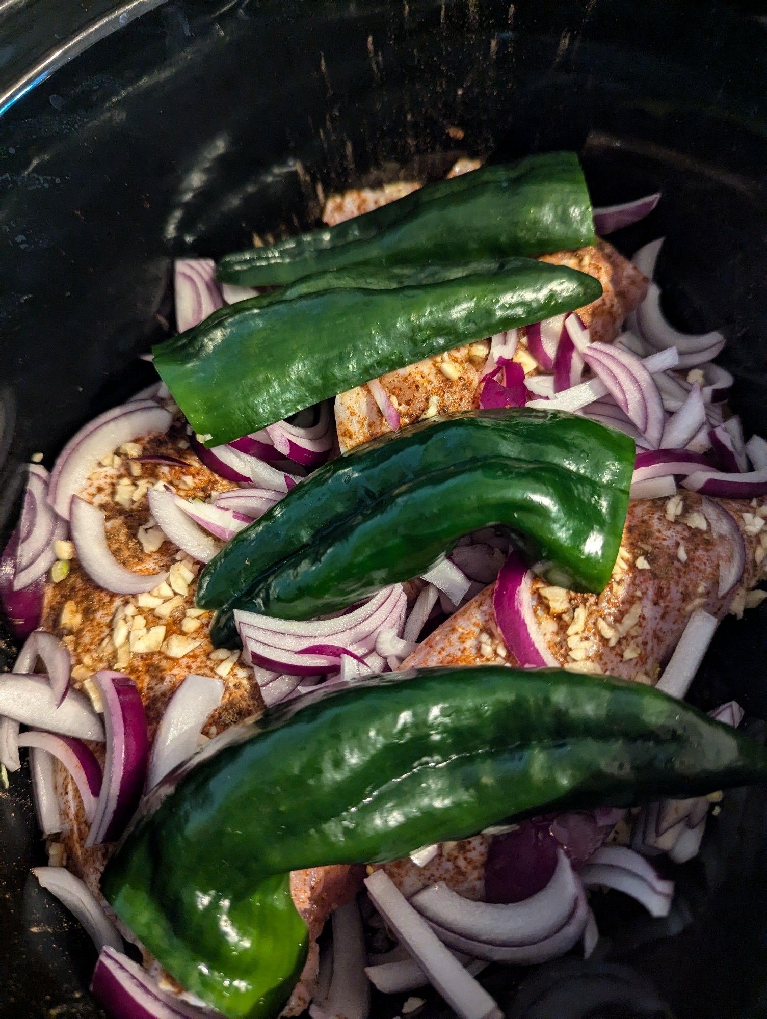 Seasoned rabbit pieces in a crock pot in with minced garlic, sliced red onion, and halves poblano peppers