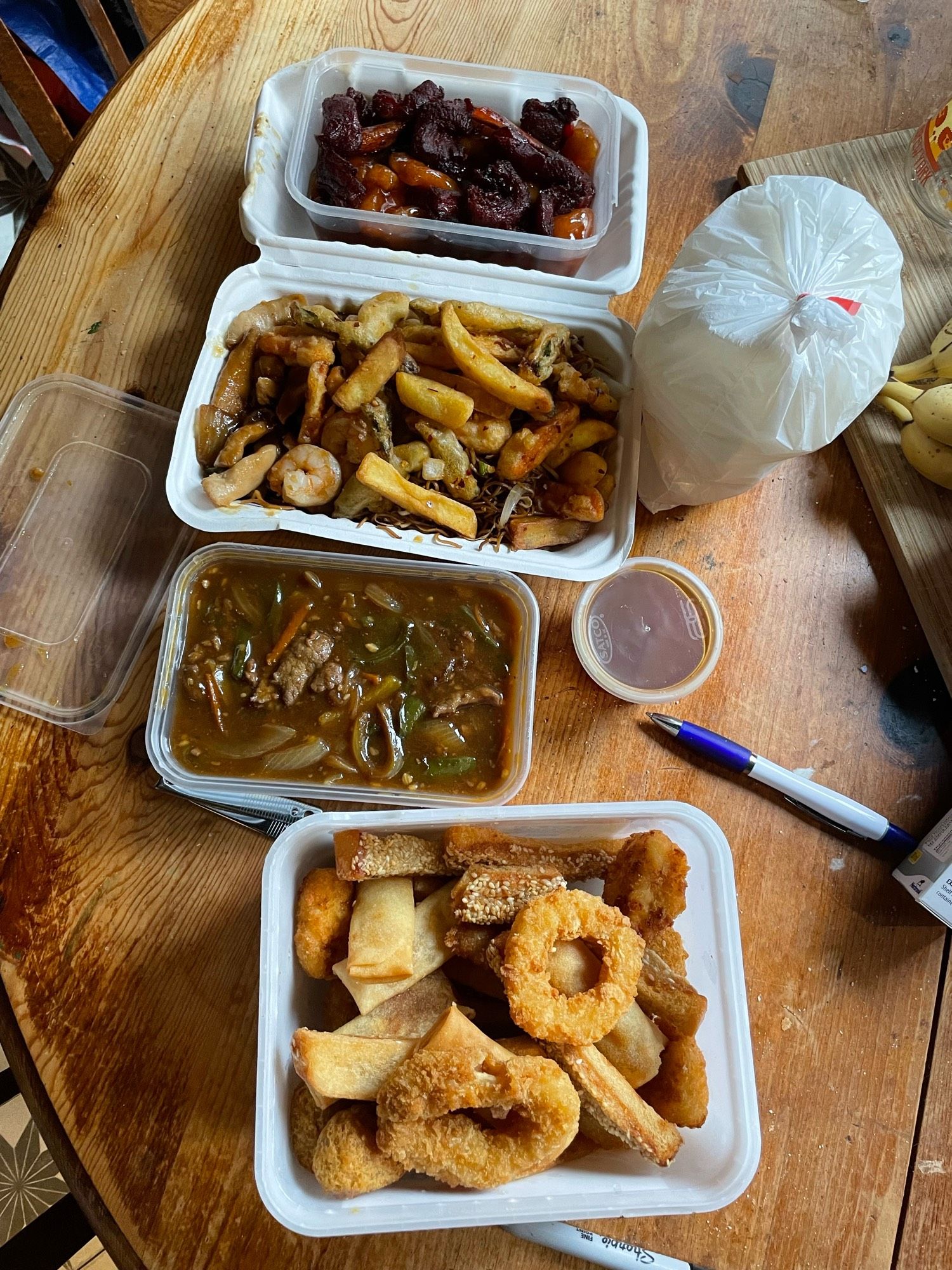 An ice cream tub of squid rings, spring rolls, chicken toast and chicken. A tub of beef with ginger and spring onion, a large box of chow mein, tempura vegetables and chips, a tub of sweet and sour chicken, and pork ribs.