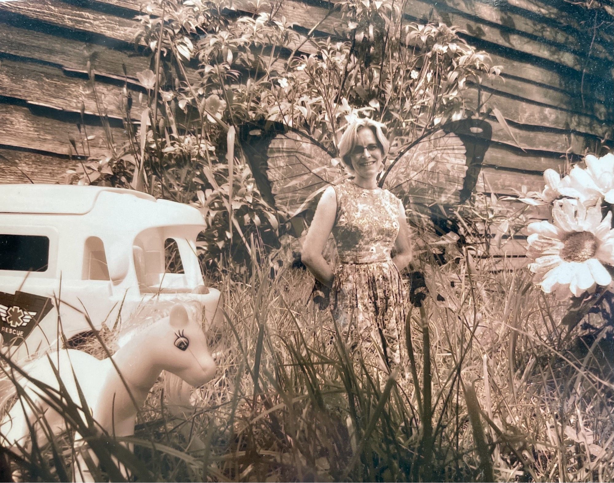 A sepia photo of a woman with wings, the same size as a My Little Pony and a Playmobil campervan.