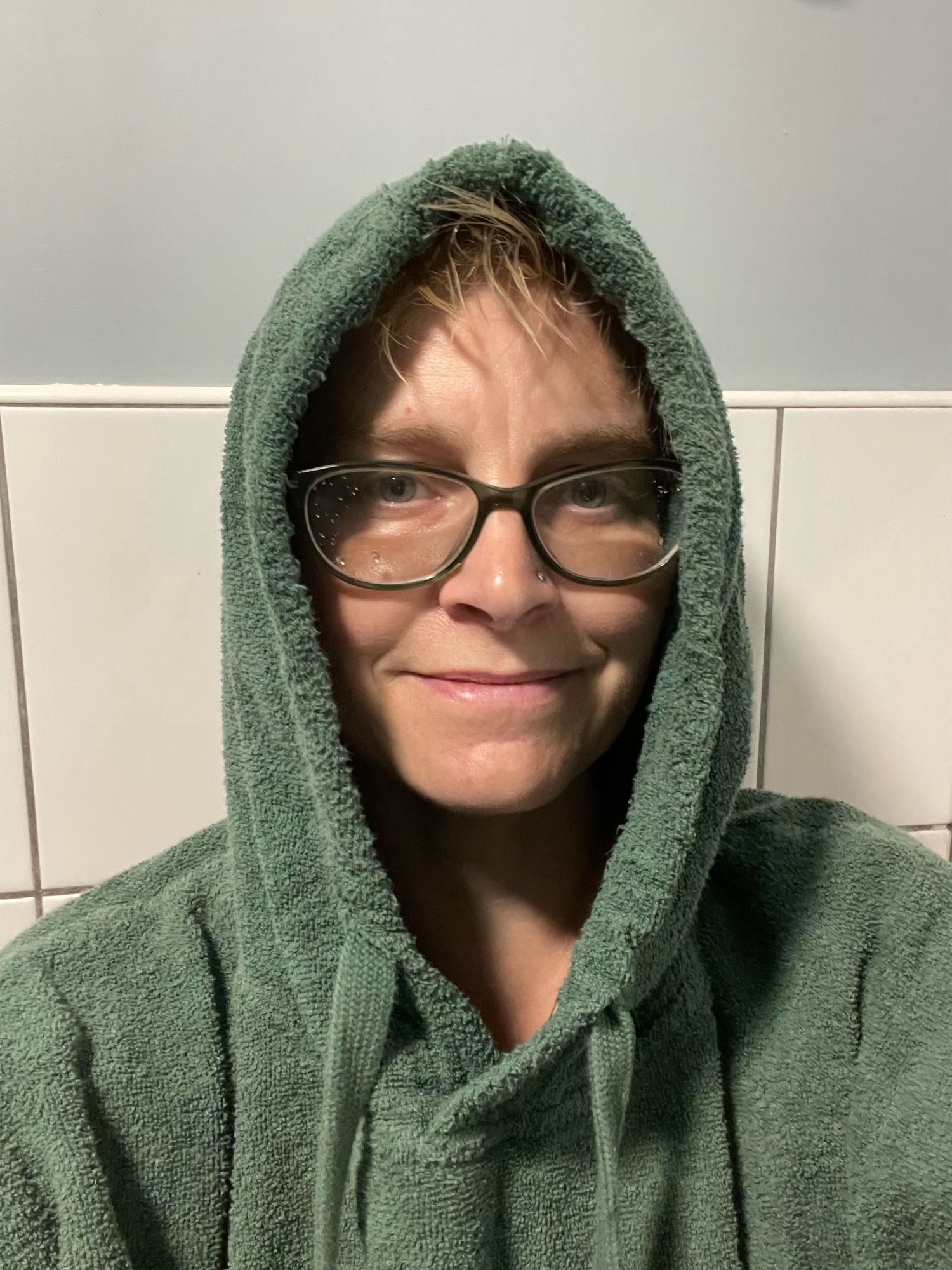 A woman with glasses wearing a hooded towel robe with the hood up. Looking tired.