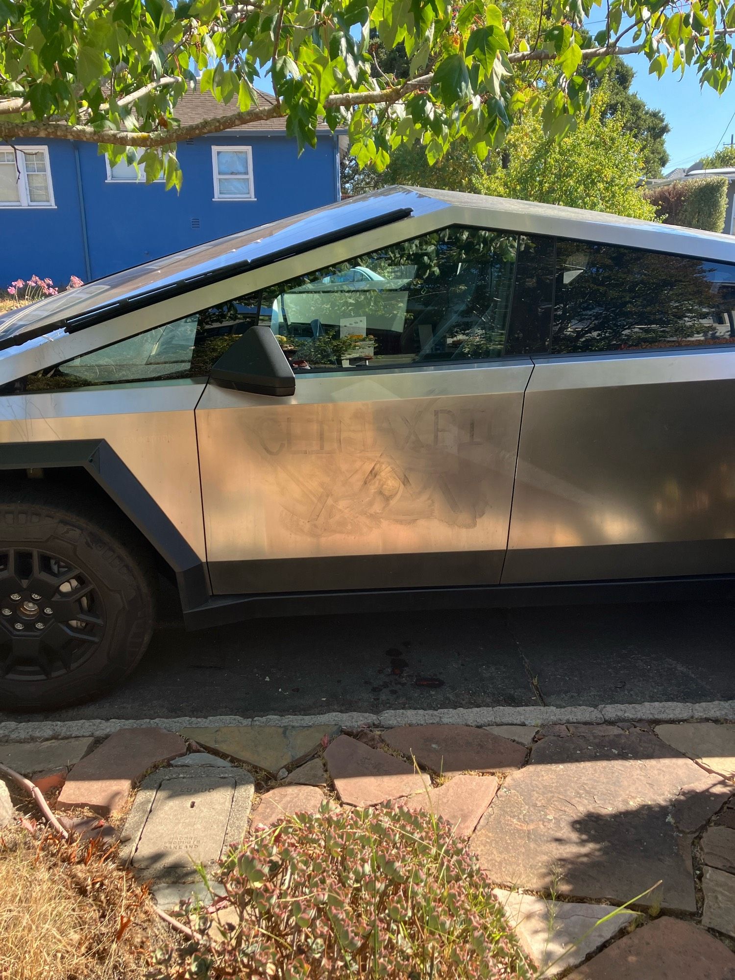 Photo of a Tesla cybertruck with the words “climax big” graffitied on the door, and signs of the owner’s vain attempt to eradicate the message.