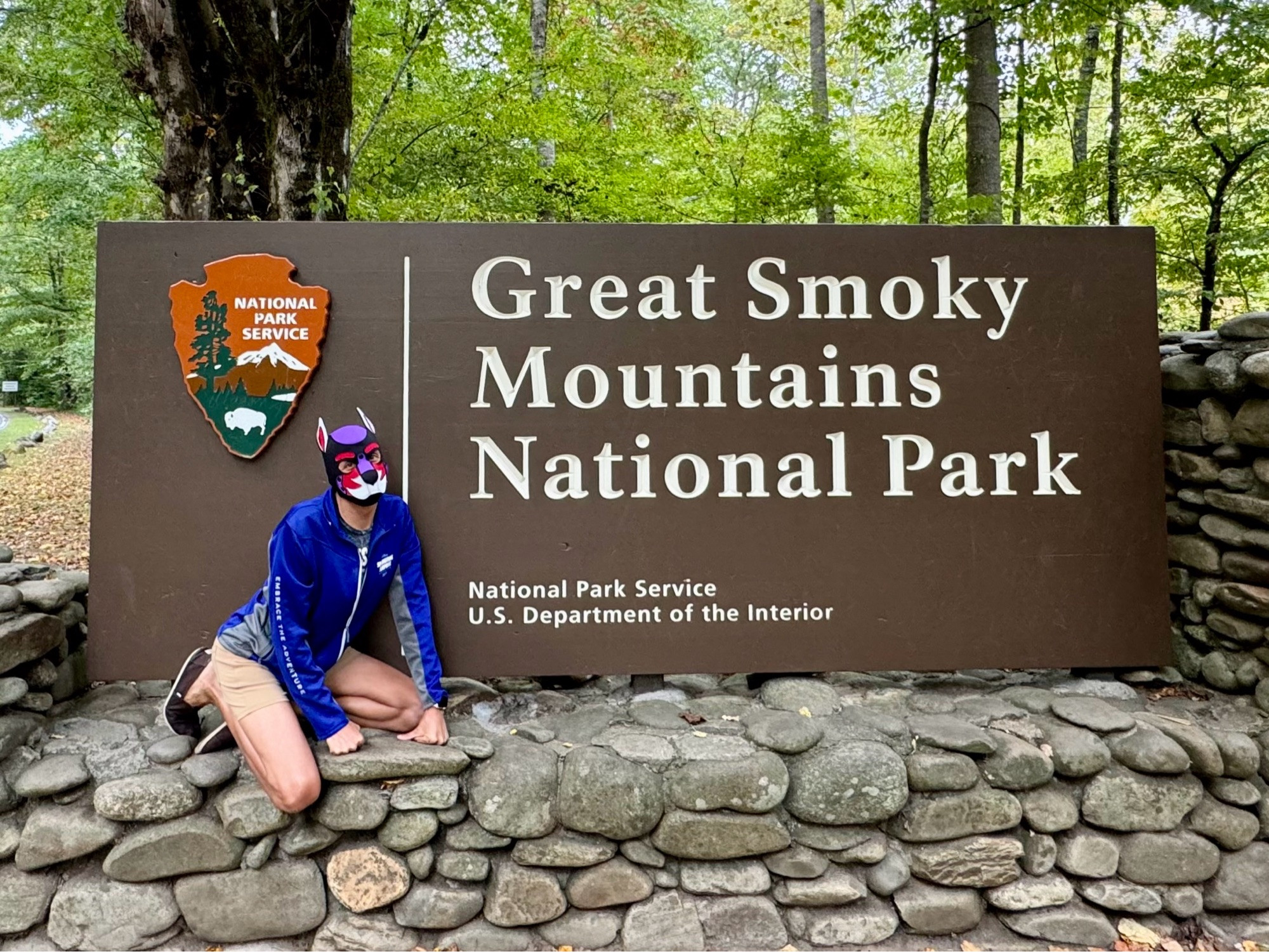 A human pup on all fours in front of the Great Smoky Mountains National Park welcome sign.