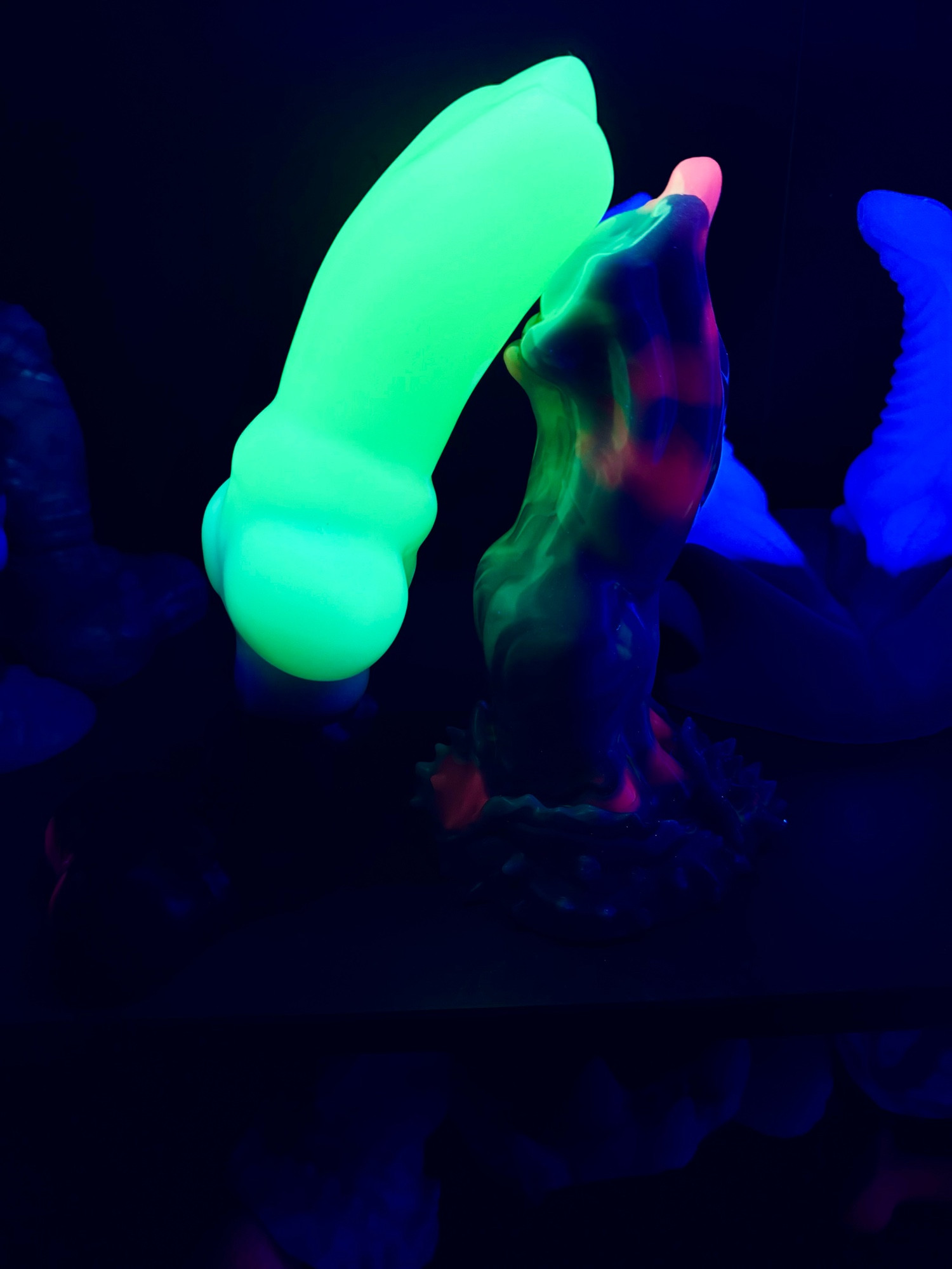 The same toys, but under UV. The canine toy glows bright green while the other toy only glows in some pink areas, and not nearly as bright as the other. 