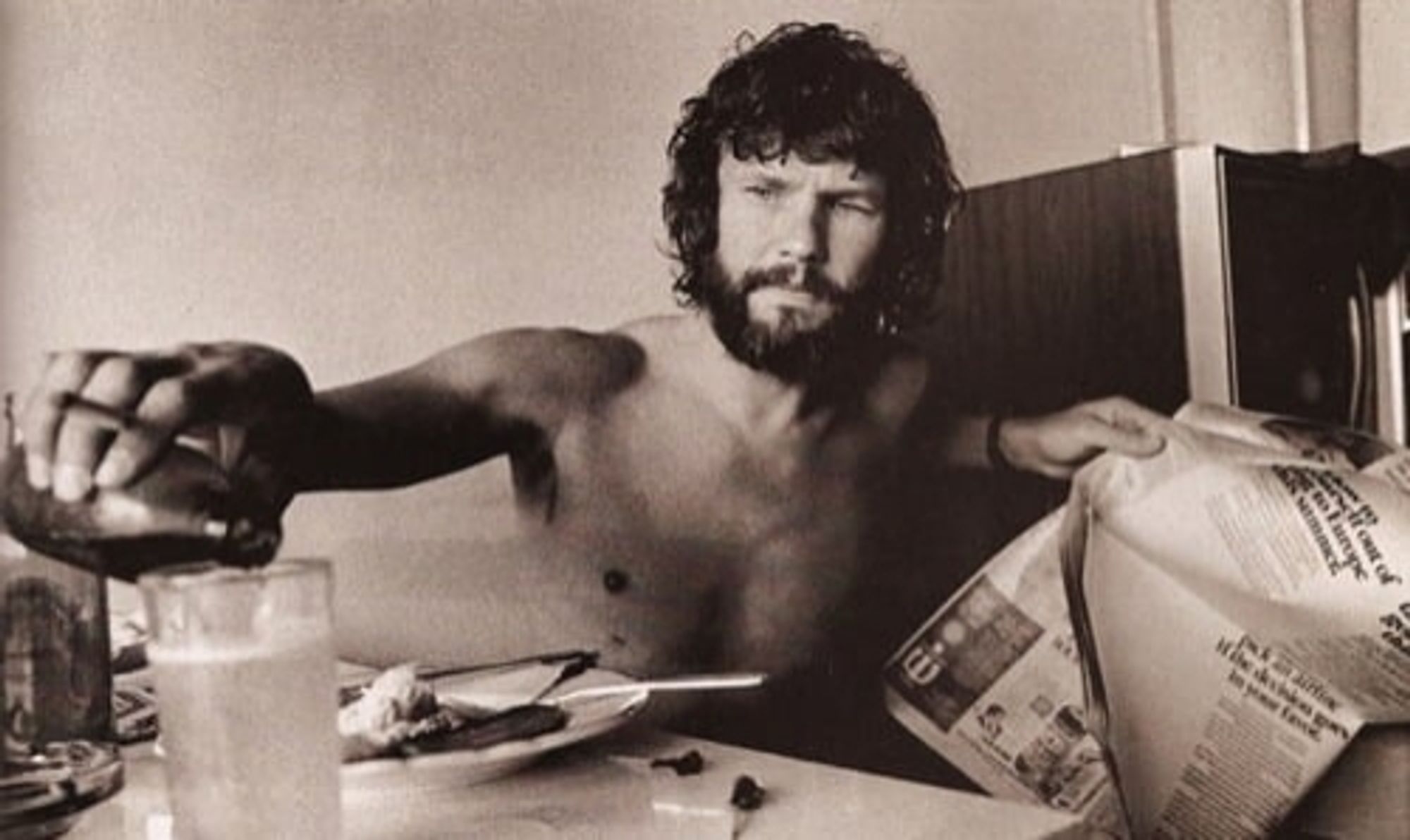 kris kristofferson shirtless having beer and reading the paper