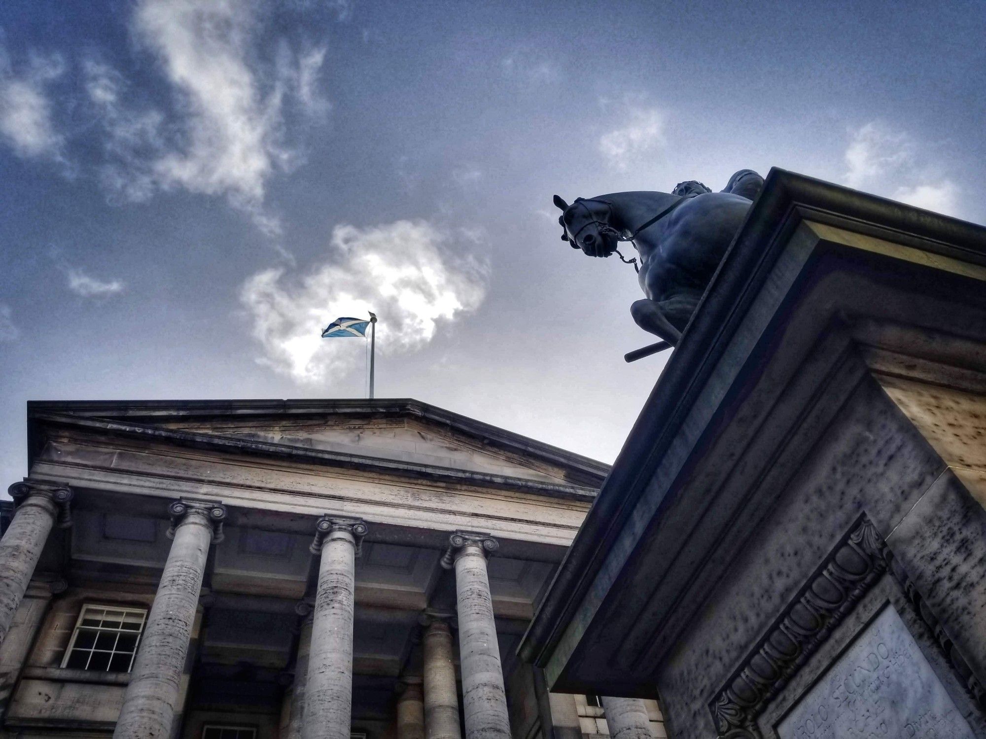 Scottish flag flies over building from below overlooking horsey statue