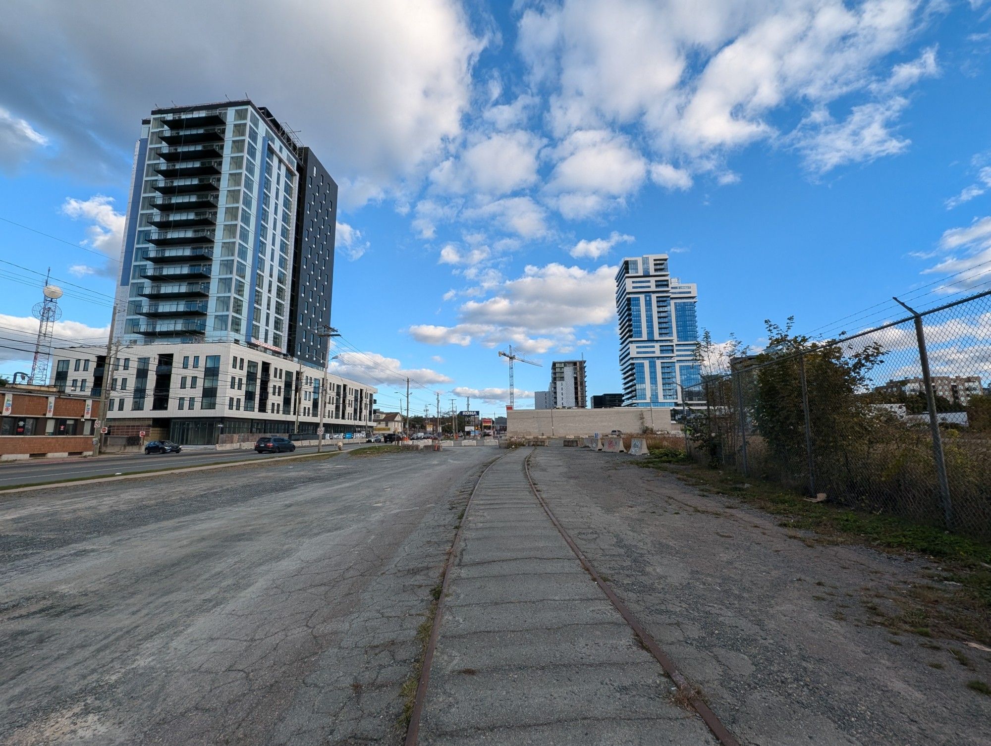 Disused segment of railway line embedded in an asphalt lot next to Robie Street, opposite the low brick CTV Atlantic tv studio. The empty lot is surrounded by several new residential high-rises.