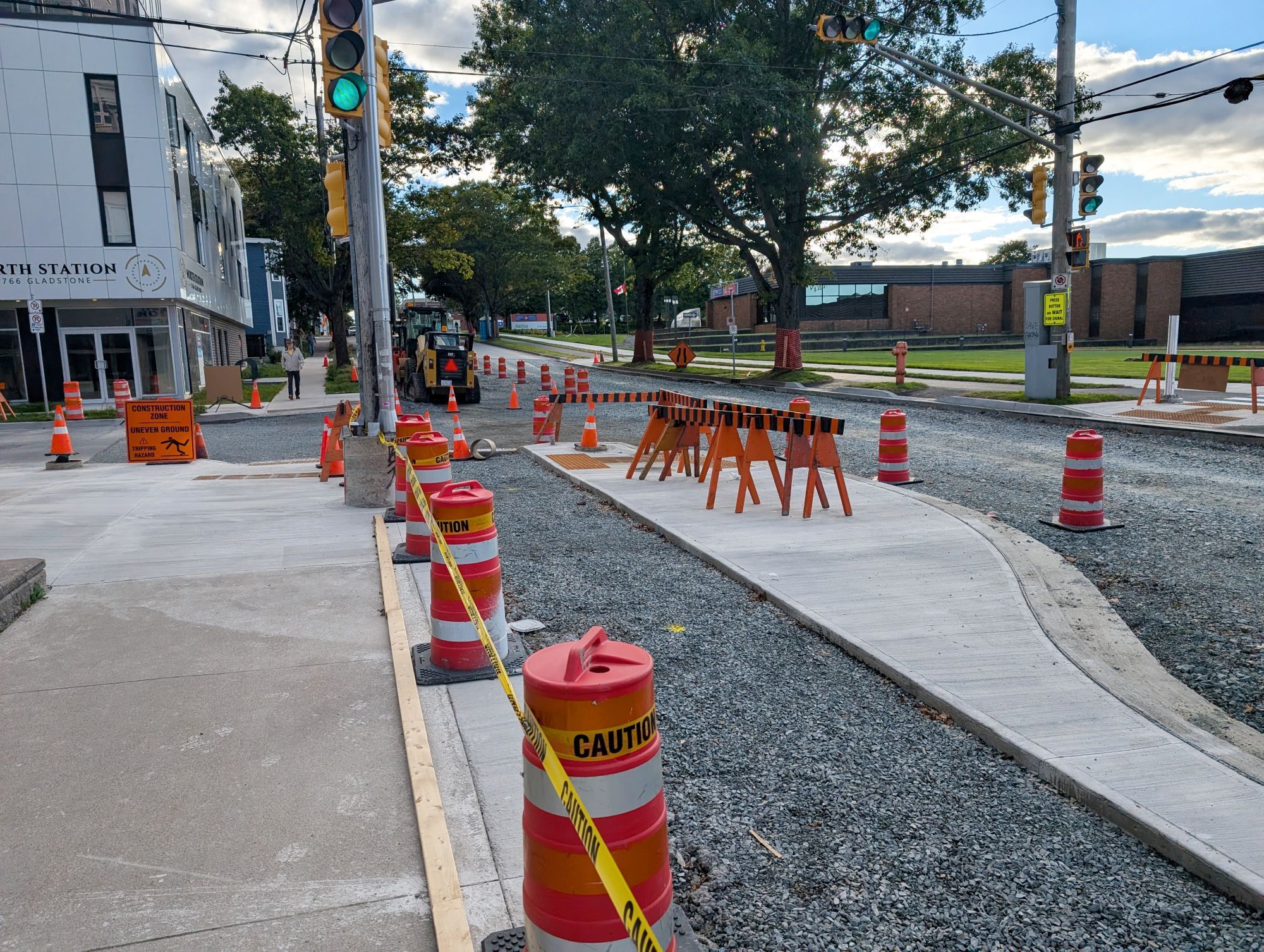 Another view of the same bike lane under construction, showing the intersection of Almon and Gladstone. The sidewalk is mostly clear aside from some cones and signage next to the crosswalk across Gladstone Street. The crosswalk across Almon Street is blocked by construction barriers.