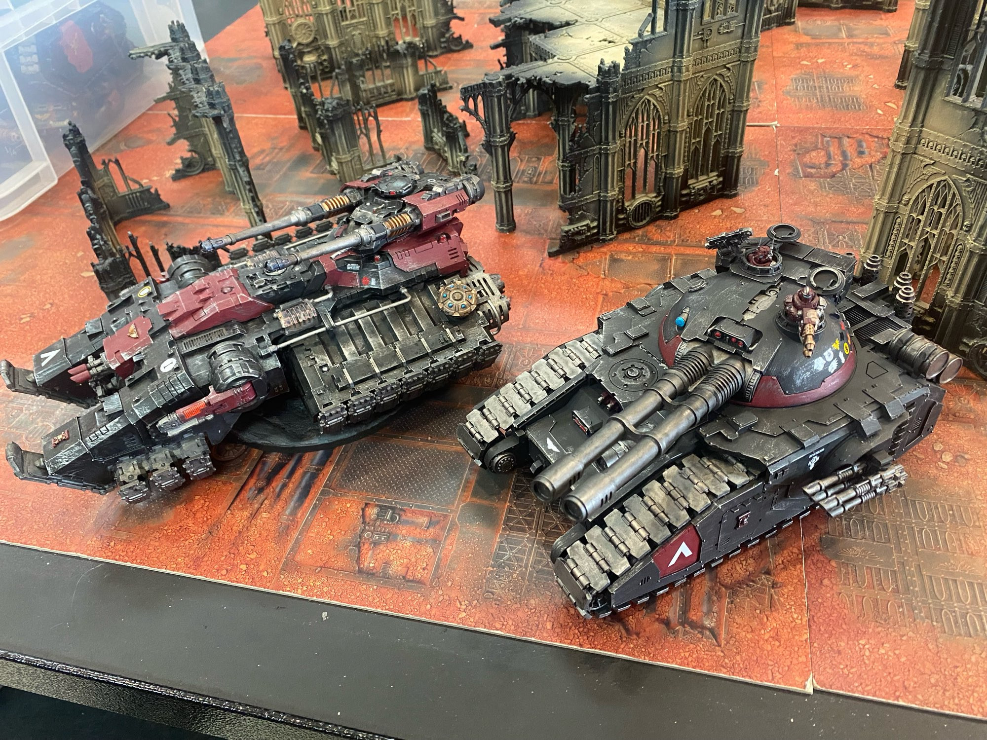 A Primaris Astraeus Super-Heavy Tank (left) sitting alongside a Fellblade Super-Heavy Tank (right), both painted as Deathwatch