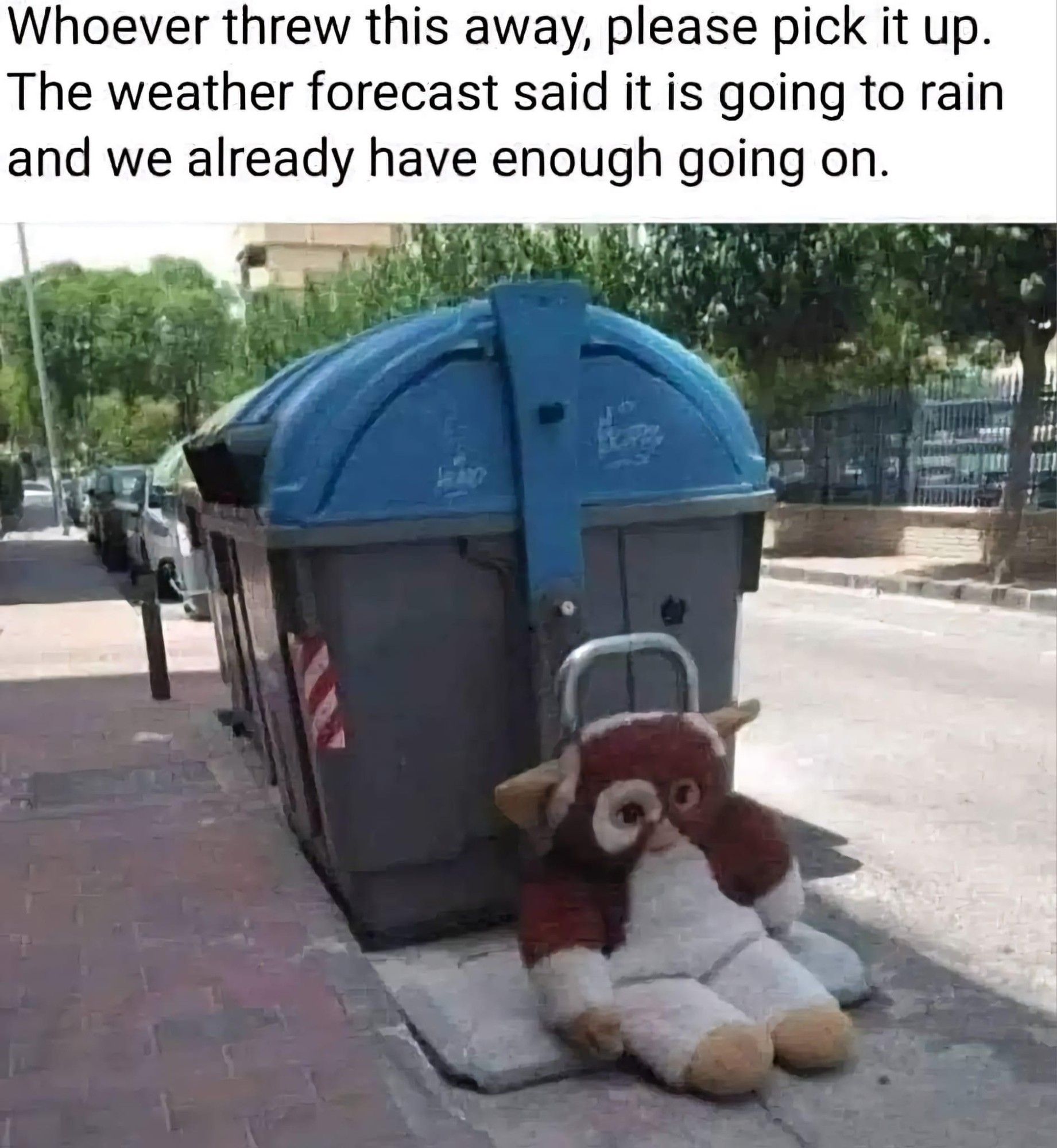 A large, stuffed animal of Gizo from the Gremlins franchise. It's outside, leaning against a trash can, abandoned. It's a bright, sunny day out.

At the top, it reads, "Whoever thres this away, please pick it up. The weather forecast said it is going to rain and we already have enough going on."