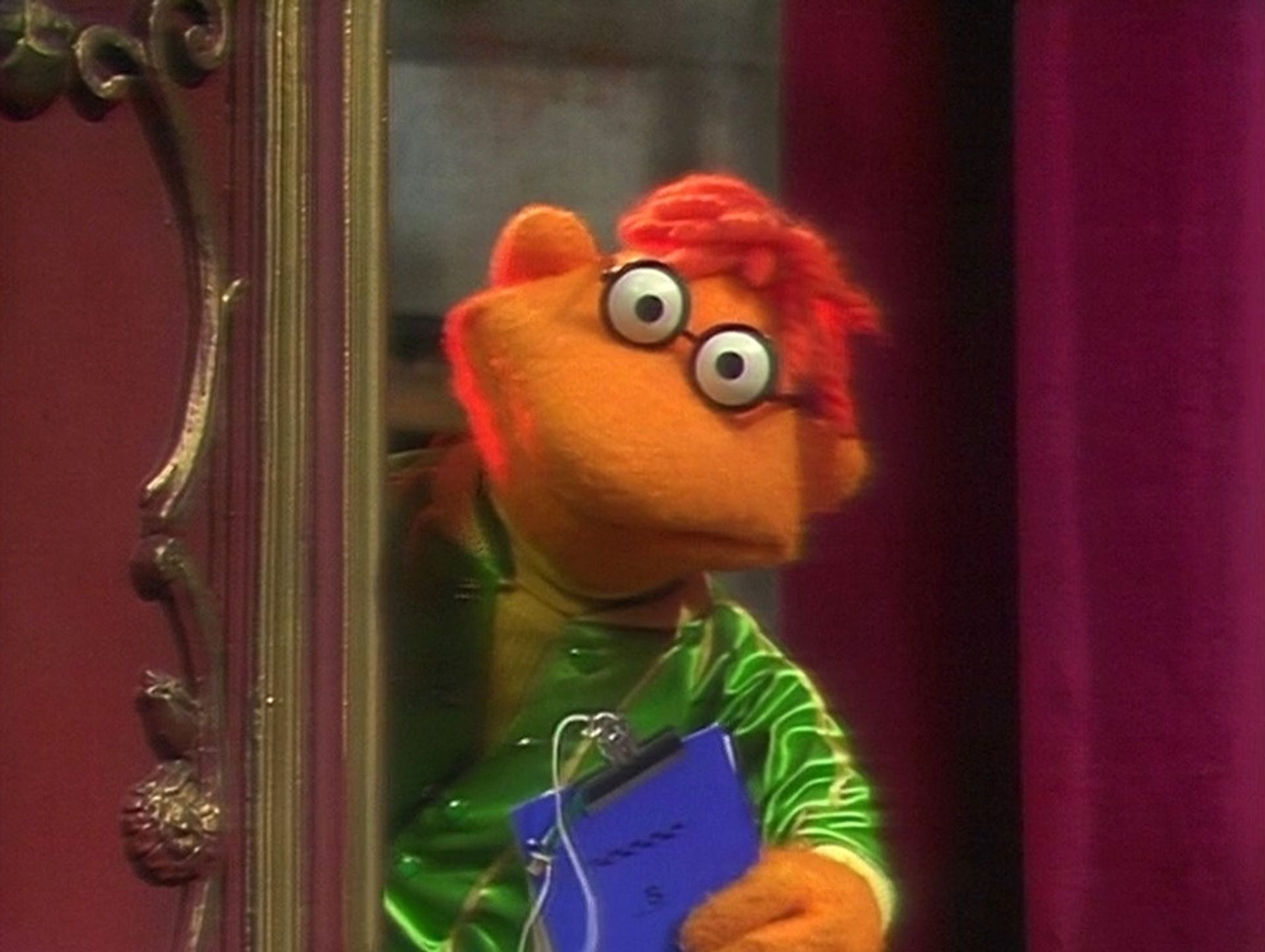 An image of Scooter from The Muppets looking around a door with a clipboard in his hand.