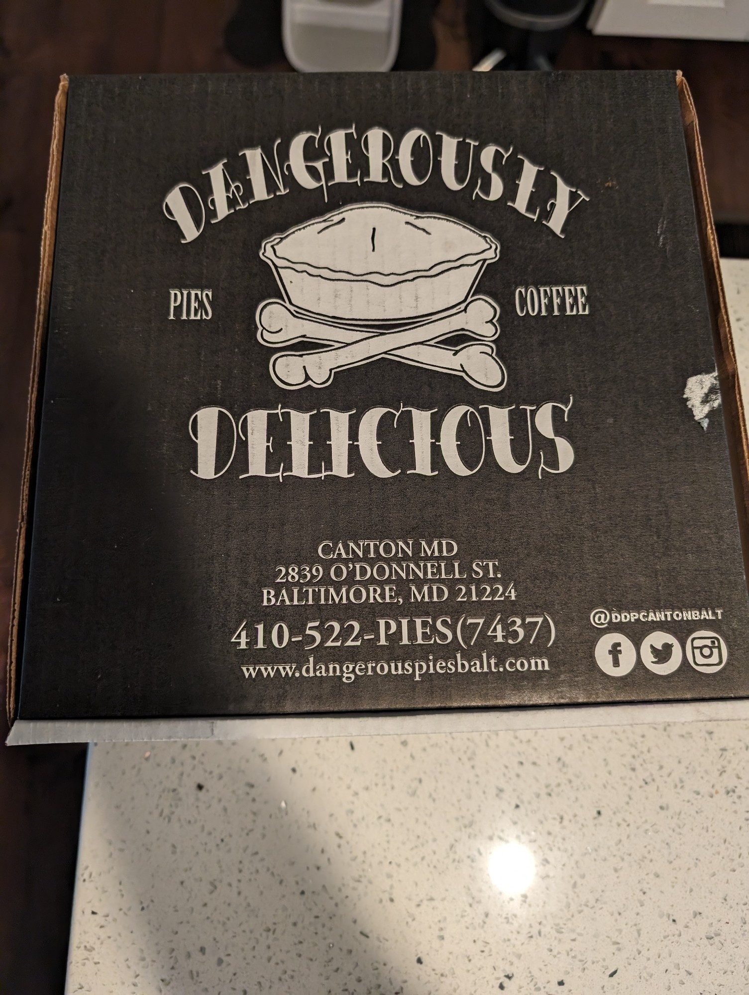 A box for Dangerously Delicious pie. It is a black box with white print.

The logo is a pie and crossbones. 

Pro tip. If you are ever flying with a DD pie, may I suggest you stay away from The Baltimore Bomb and stick with a more traditional pie. Without fail, TSA will ask you what type of pie you have and a Baltimore Bomb will make flying awkward.