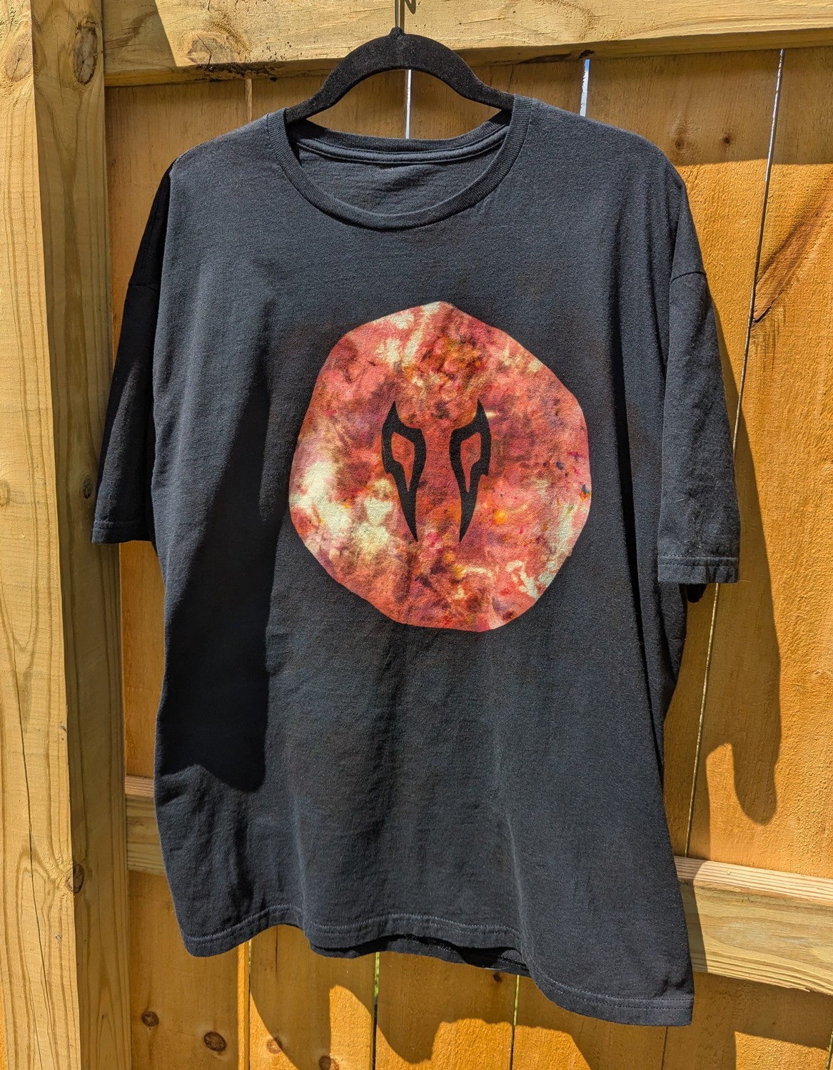 A black reverse-dyed shirt with a Viper crystal symbol from FFXIV, colored in with rust-colored scrunch ice-dye. 