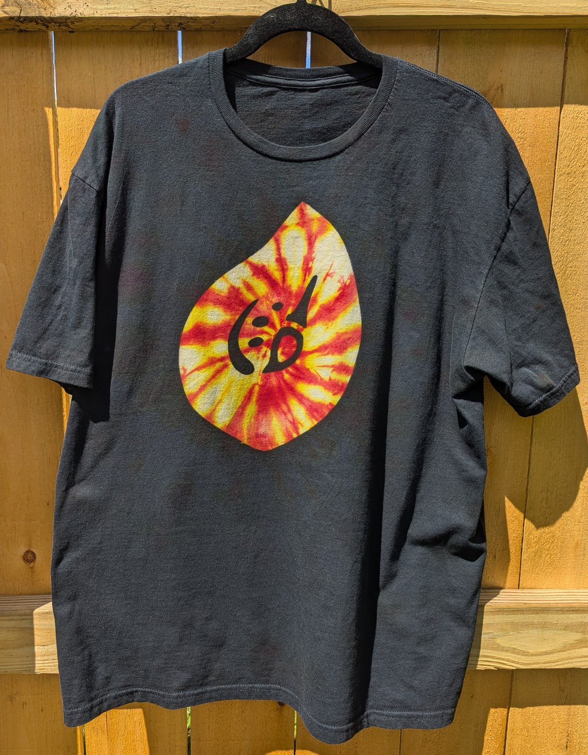 A black reverse-dyed shirt with a Pictomancer crystal symbol from FFXIV, colored in with yellow and red spiral ice-dye.