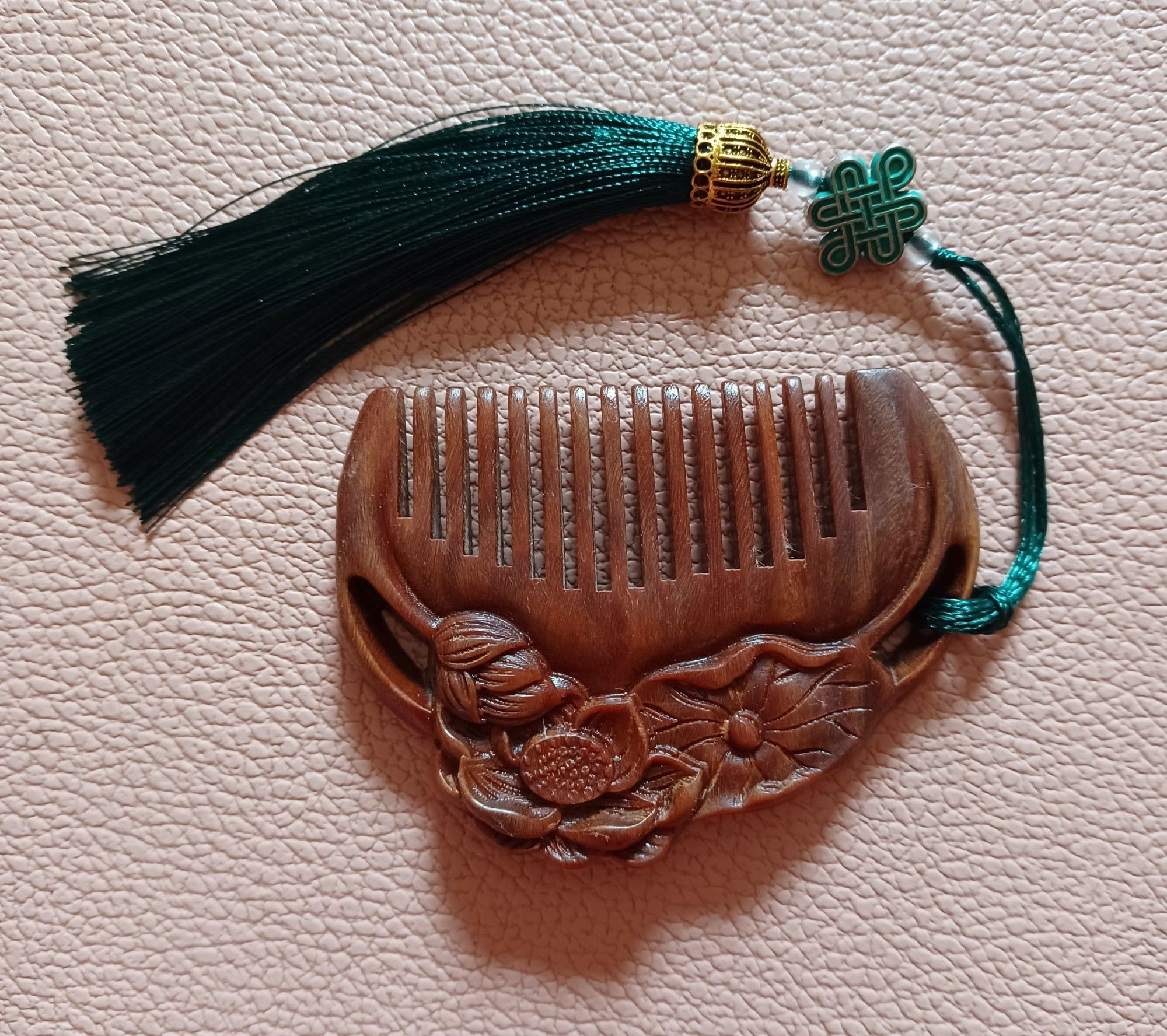 A small comb made of sandalwood. It features lotus blooms and leaves on the back handle.