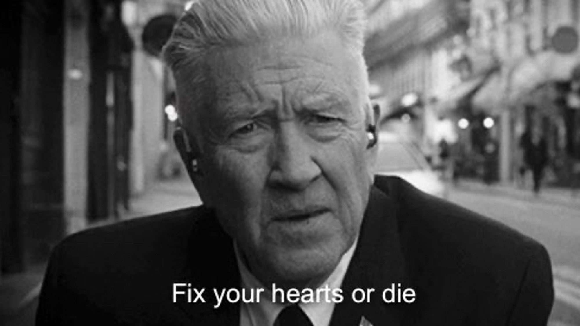 A black and white photo of David Lynch in Twin Peaks, with the subhead “Fix your hearts or die”