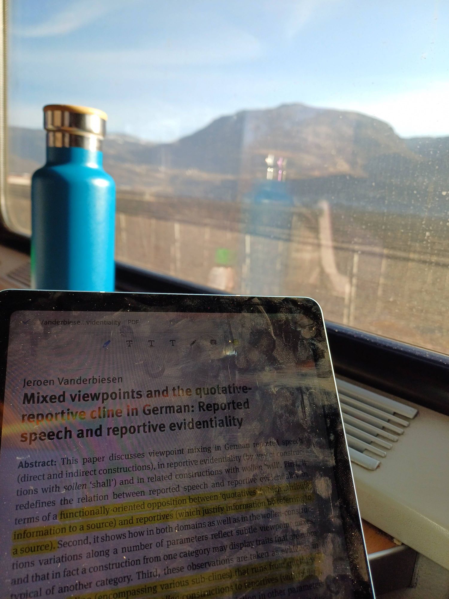 Tablet displaying Jeroen Vanderbiesen's paper "Mixed viewpoints and the quotative-reportive cline in German". Mountains in the background, viewed from a train window